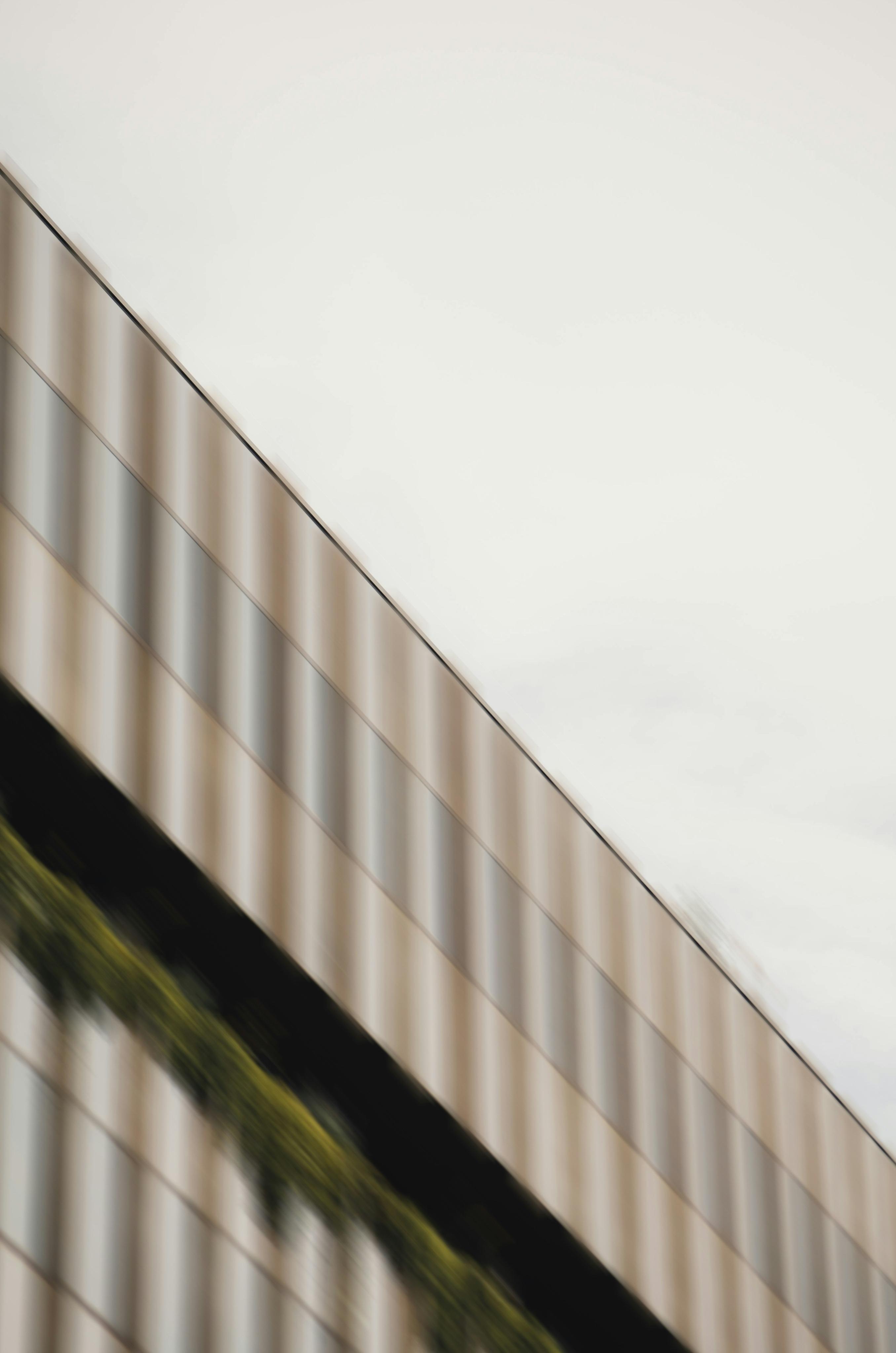 Close-up of a modern building's exterior wall with reflective glass windows and a strip of greenery, angled upwards against a pale sky.