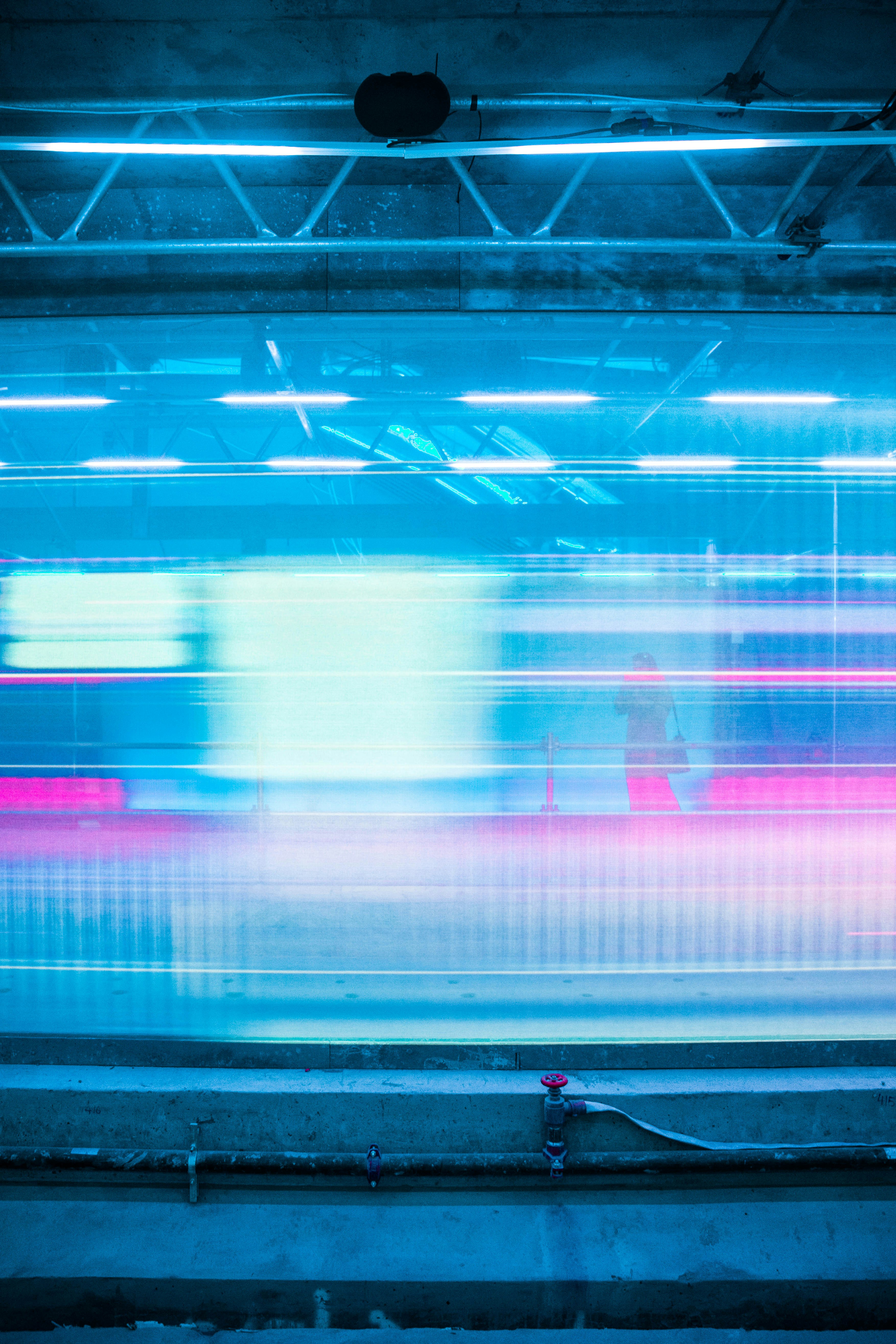 Blurred motion of a train passing in an underground station with blue and pink light streaks and a faint silhouette of a person standing on the platform.