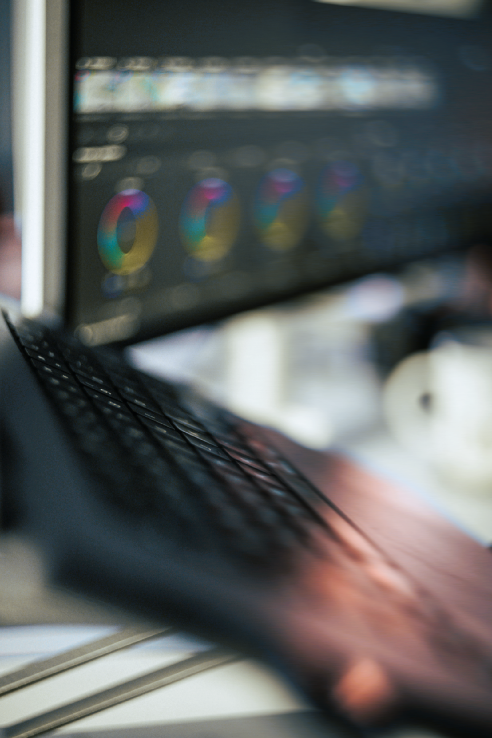Close-up of a person typing on a black laptop keyboard with a blurred monitor in the background displaying colorful circular charts and data visualizations.