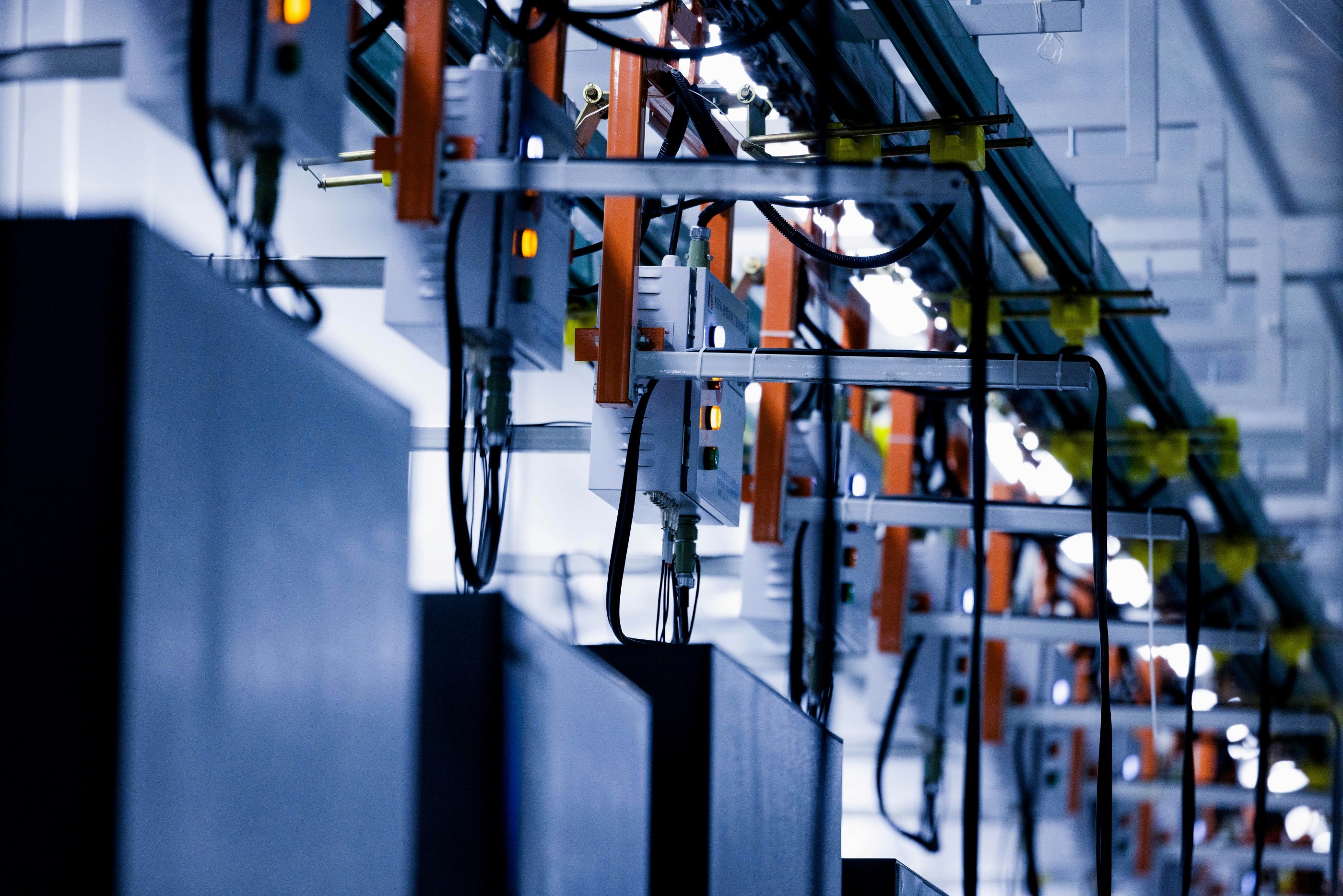 Close-up view of industrial electrical equipment and wiring mounted on orange and white metal structures along a ceiling in a factory or data center environment.