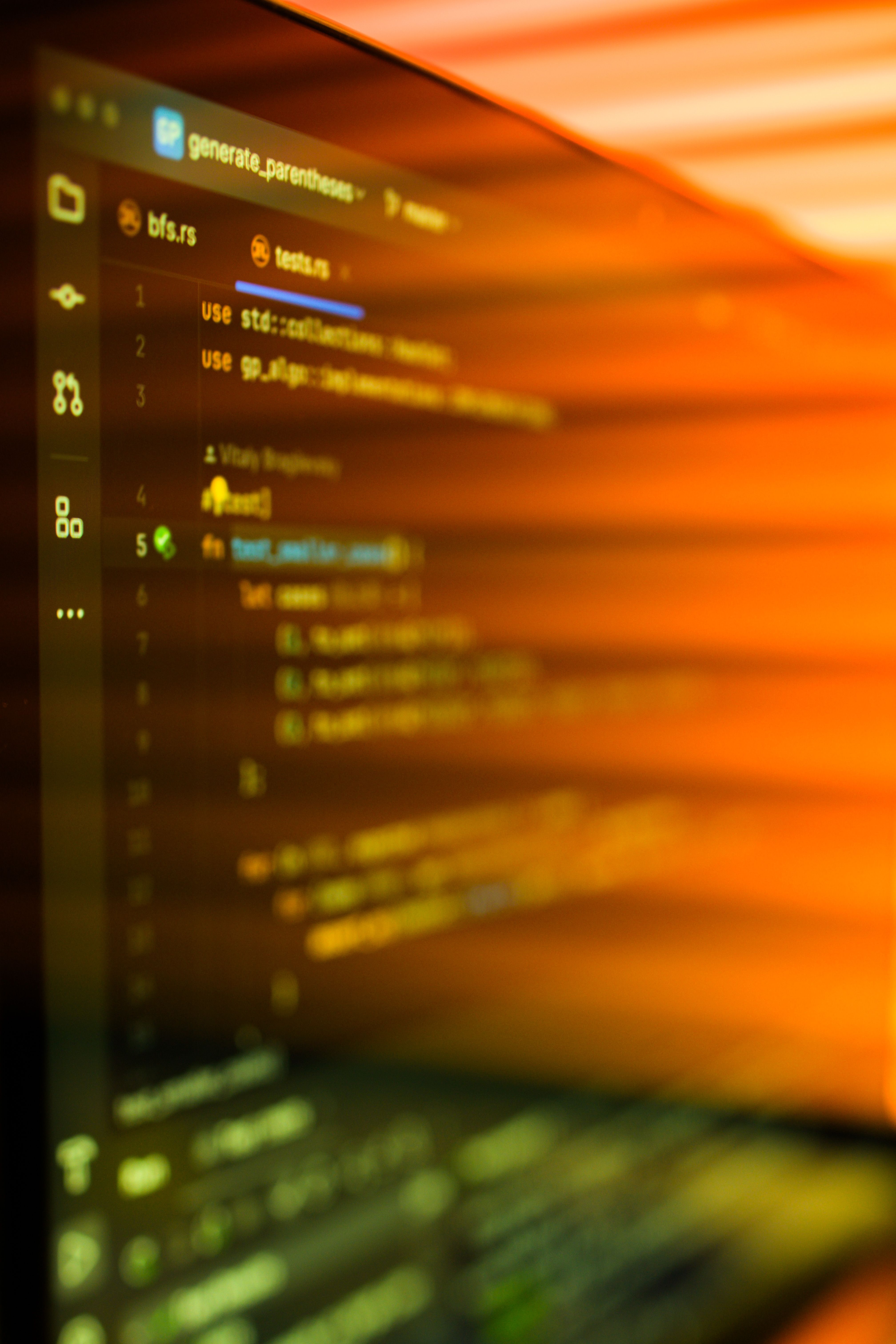 Close-up of a computer screen displaying blurred source code in a text editor with an orange light reflection.