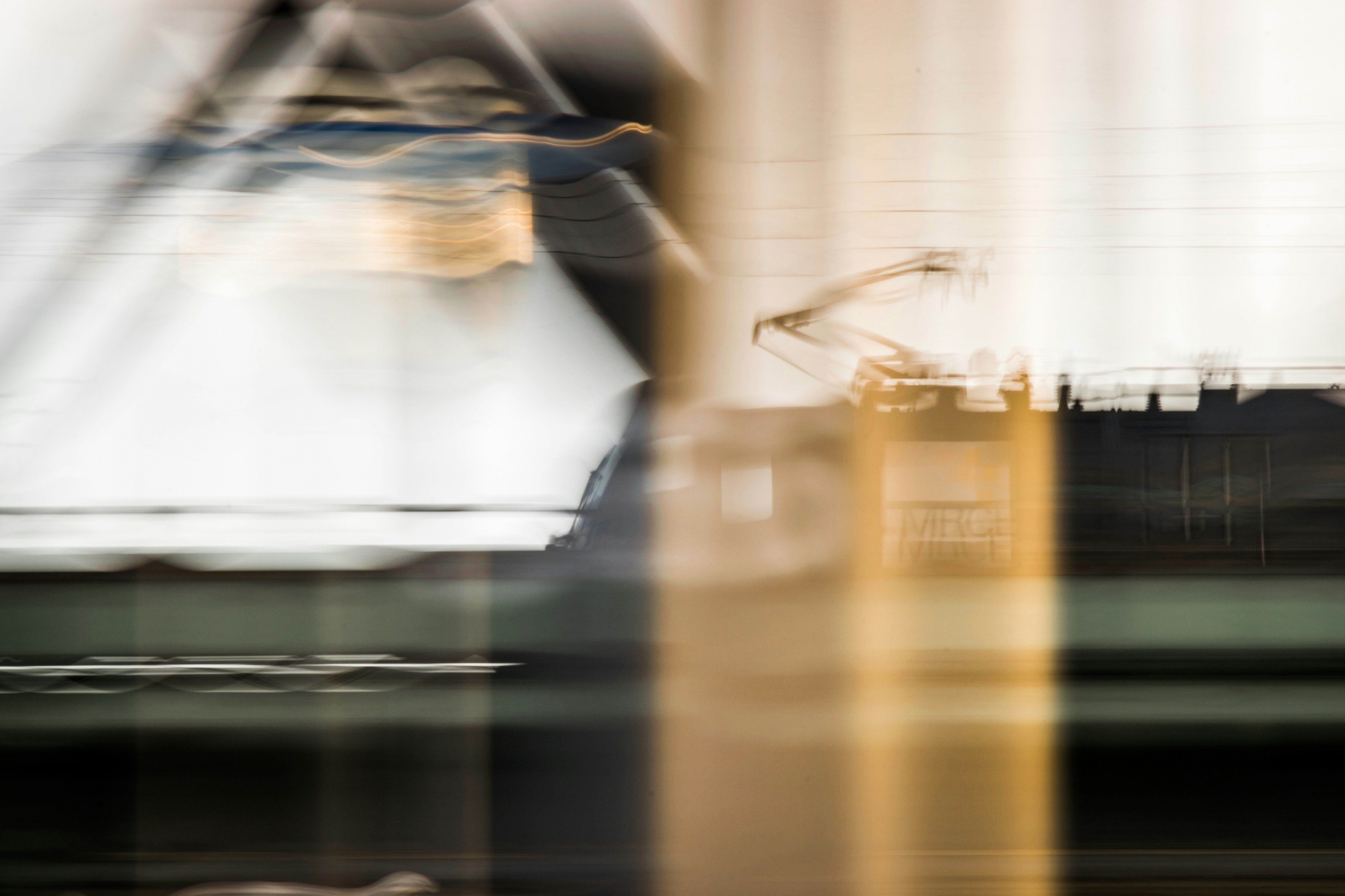 Abstract blurred image of a moving train with overhead electric lines, creating streaks of light and shapes.