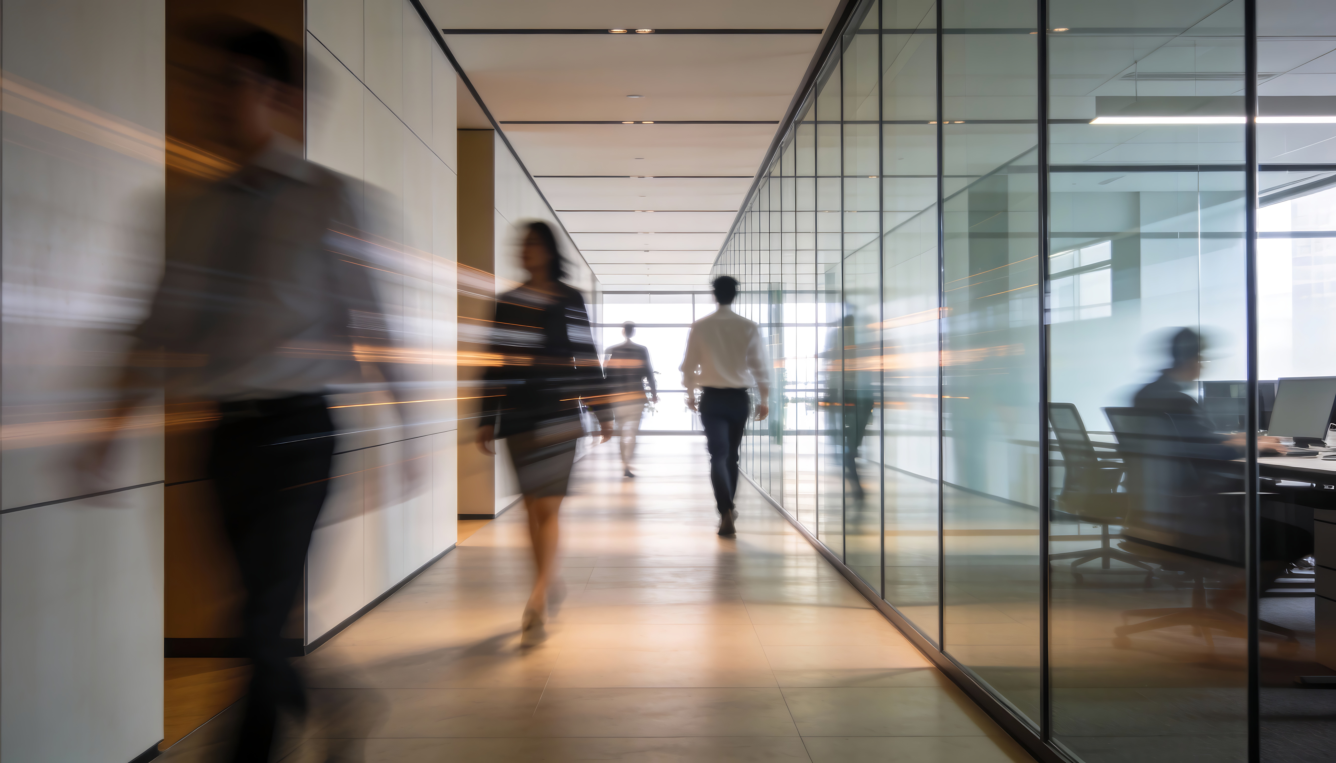 Blurred motion of people walking and working in a modern office hallway with glass walls and bright lighting.
