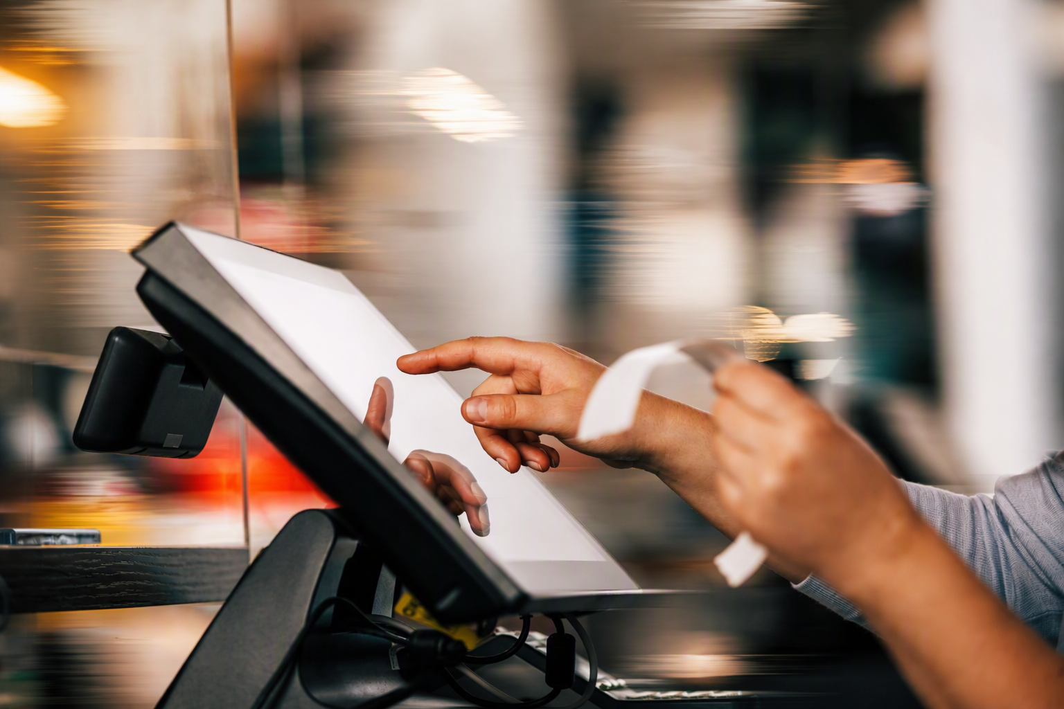 Person using a touchscreen point-of-sale system while holding a receipt in one hand and tapping the screen with the other.