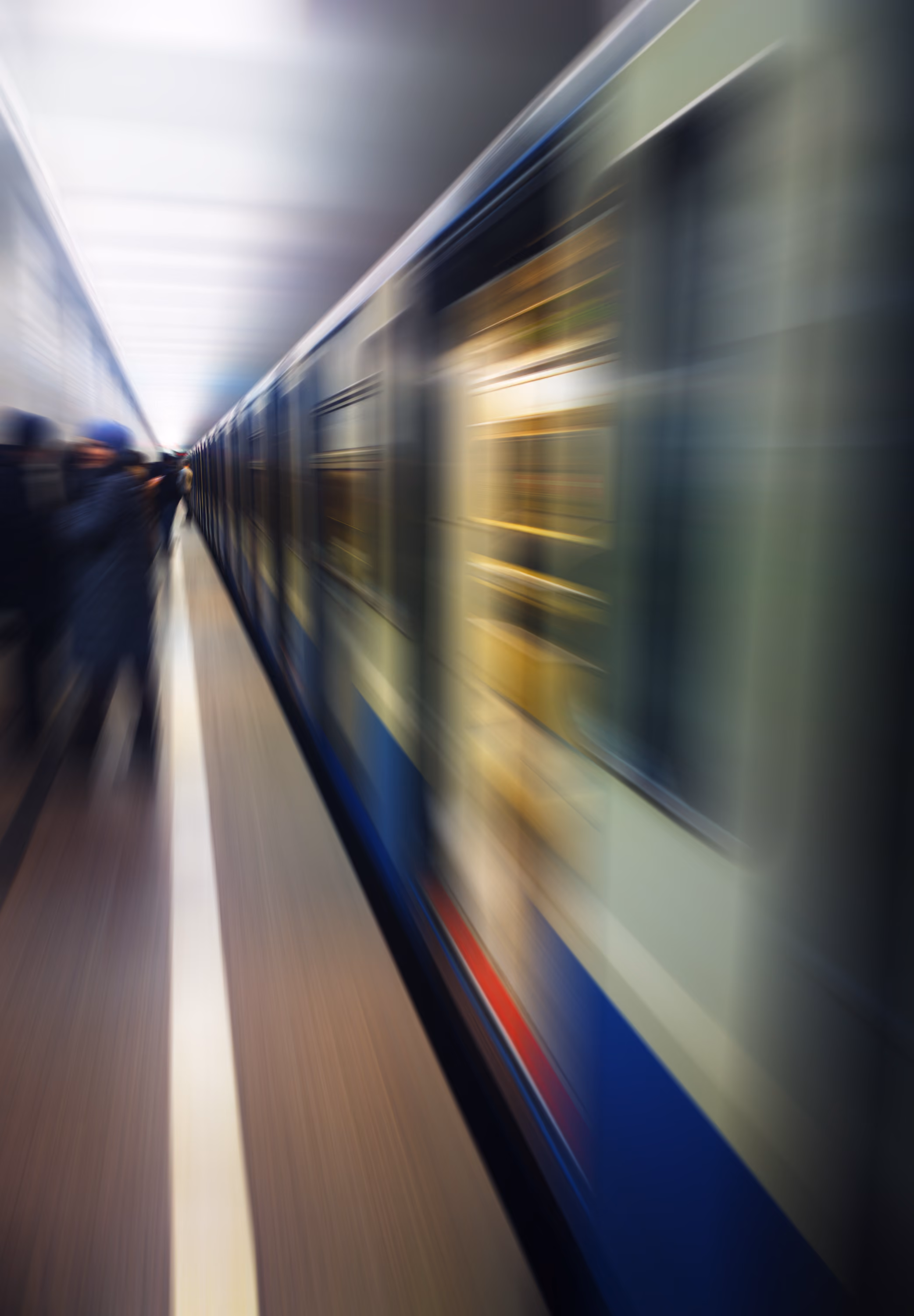 Blurred image of a subway train moving quickly through an underground station with indistinct passengers waiting on the platform.