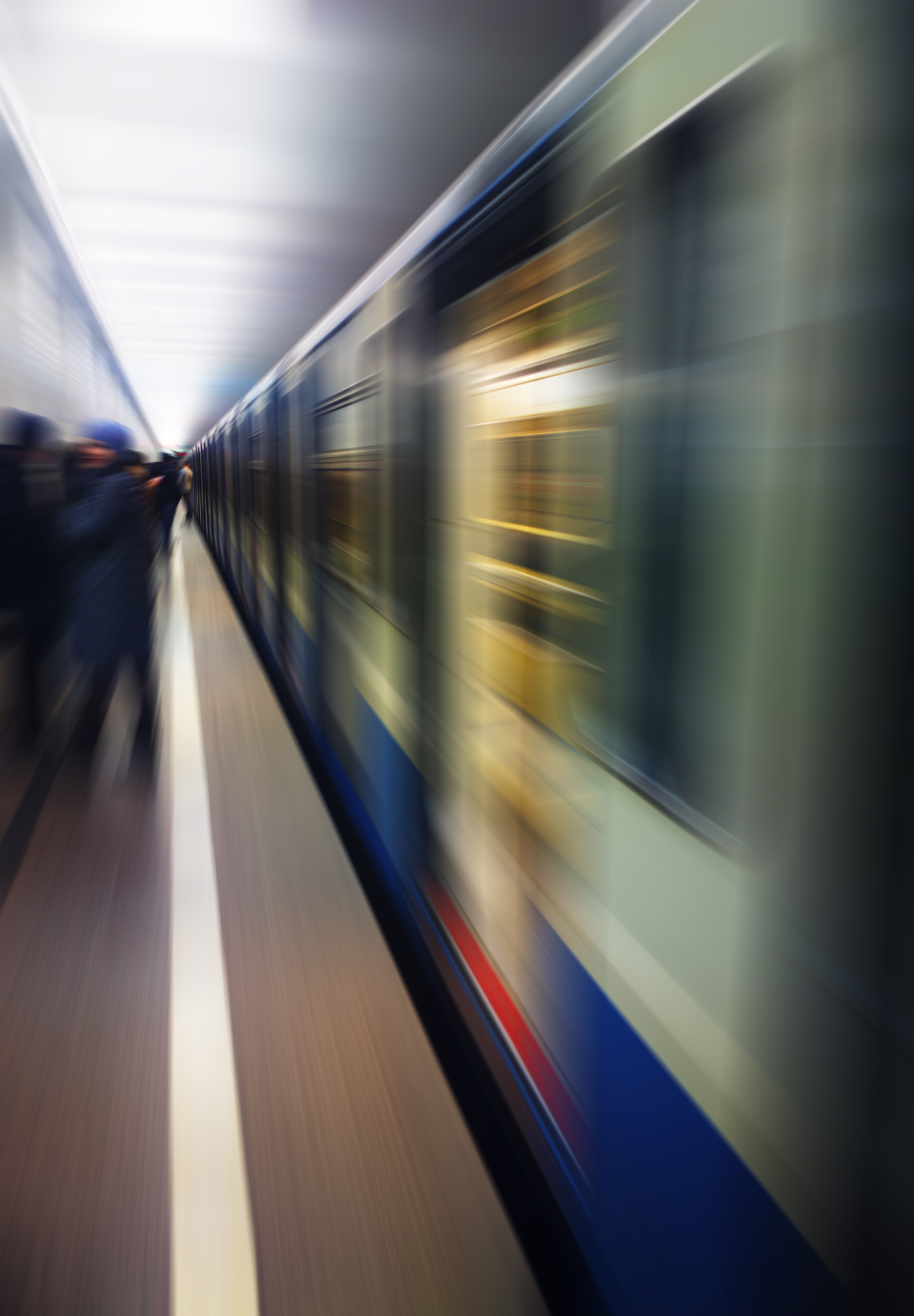 Blurred image of a subway train moving quickly through an underground station with indistinct passengers waiting on the platform.