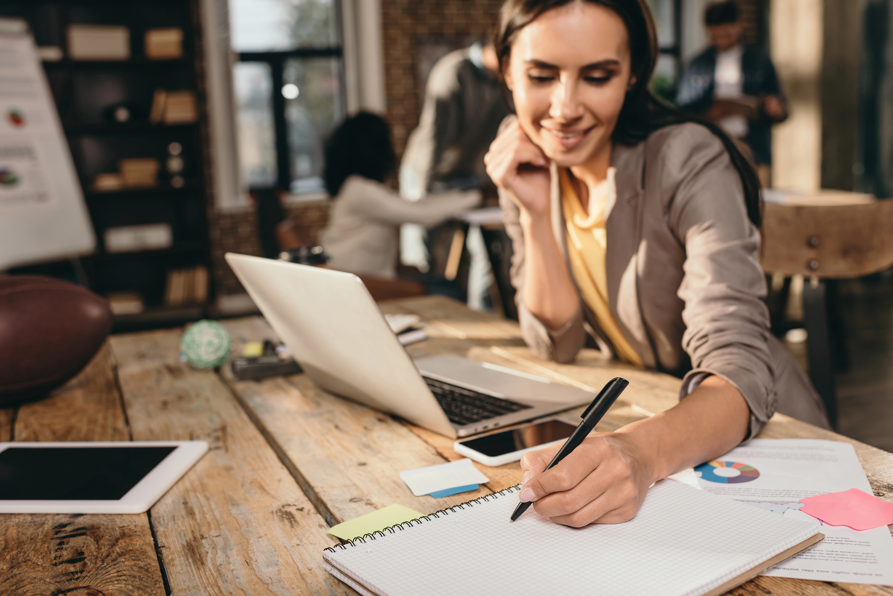 Professional wearing a headset and taking notes beside a laptop during remote work