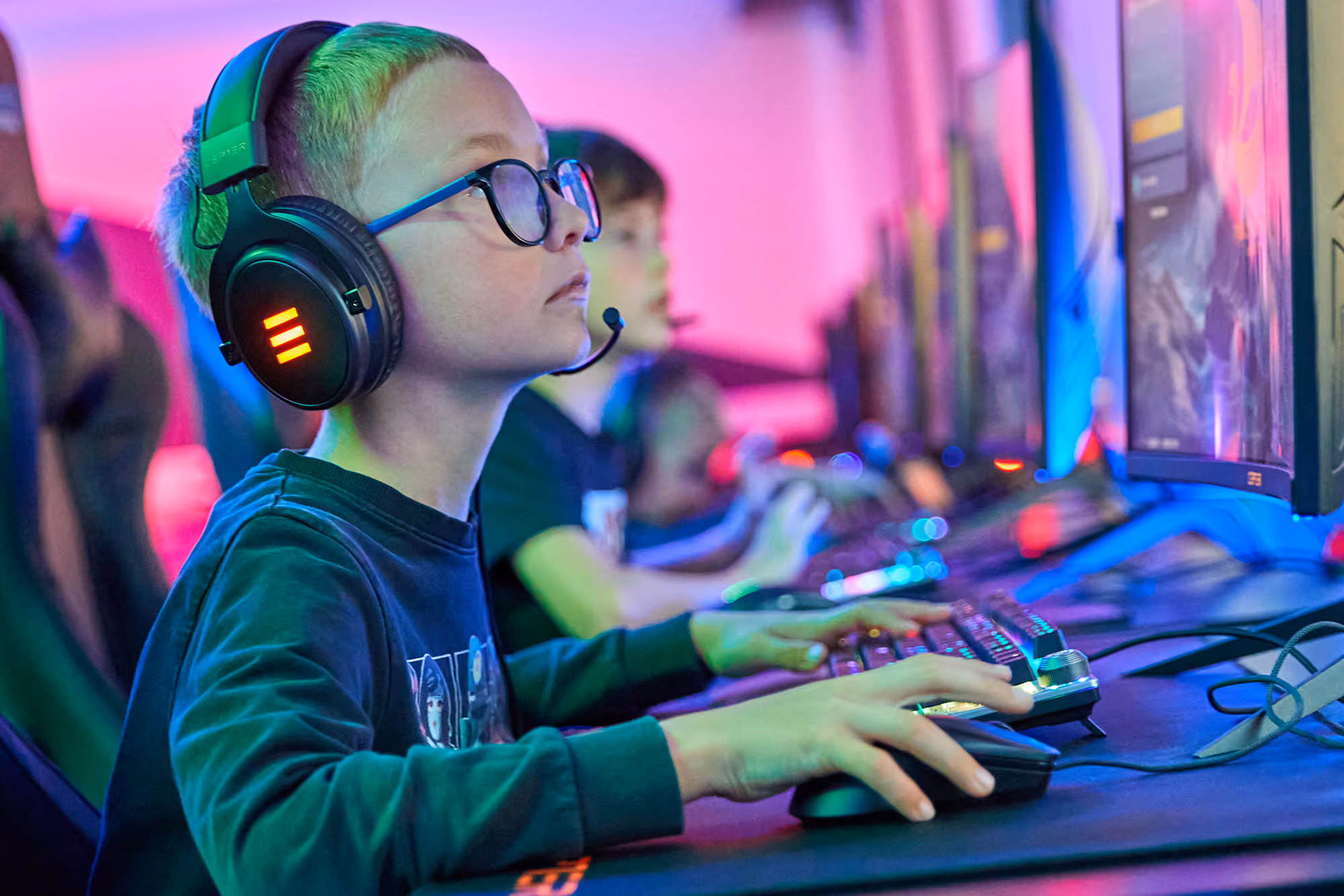 Barn med headset og briller spiller dataspill på tastatur og mus i et fargerikt rom.