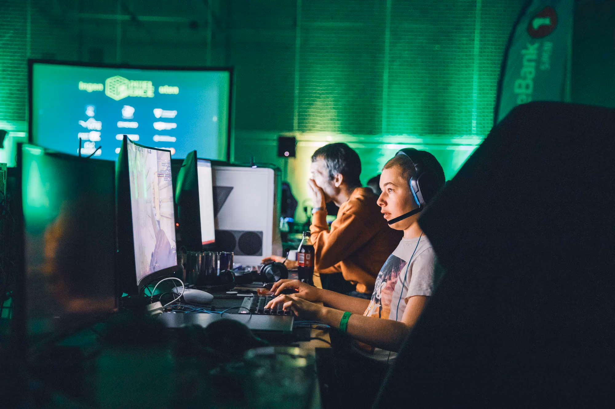 To unge personer som spiller dataspill med headset i et rom med grønt lys.