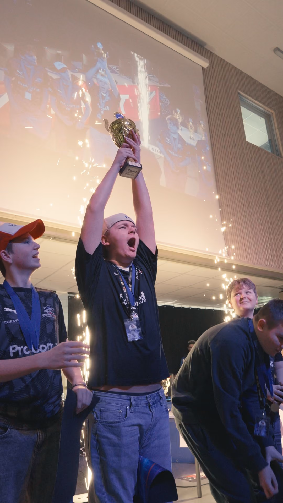 Ung gutt jubler med pokal i hendene mens venner ser på under en feiring med fyrverkeri.