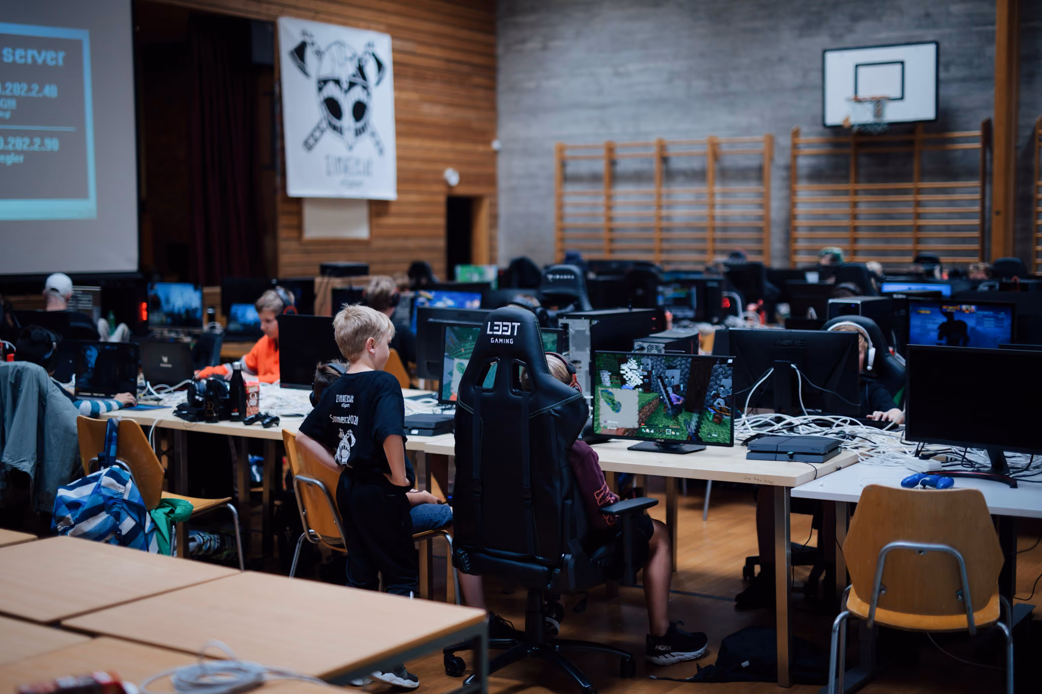 Barn spiller videospill på PC-er i et rom med trevegger og en basketballkurv.