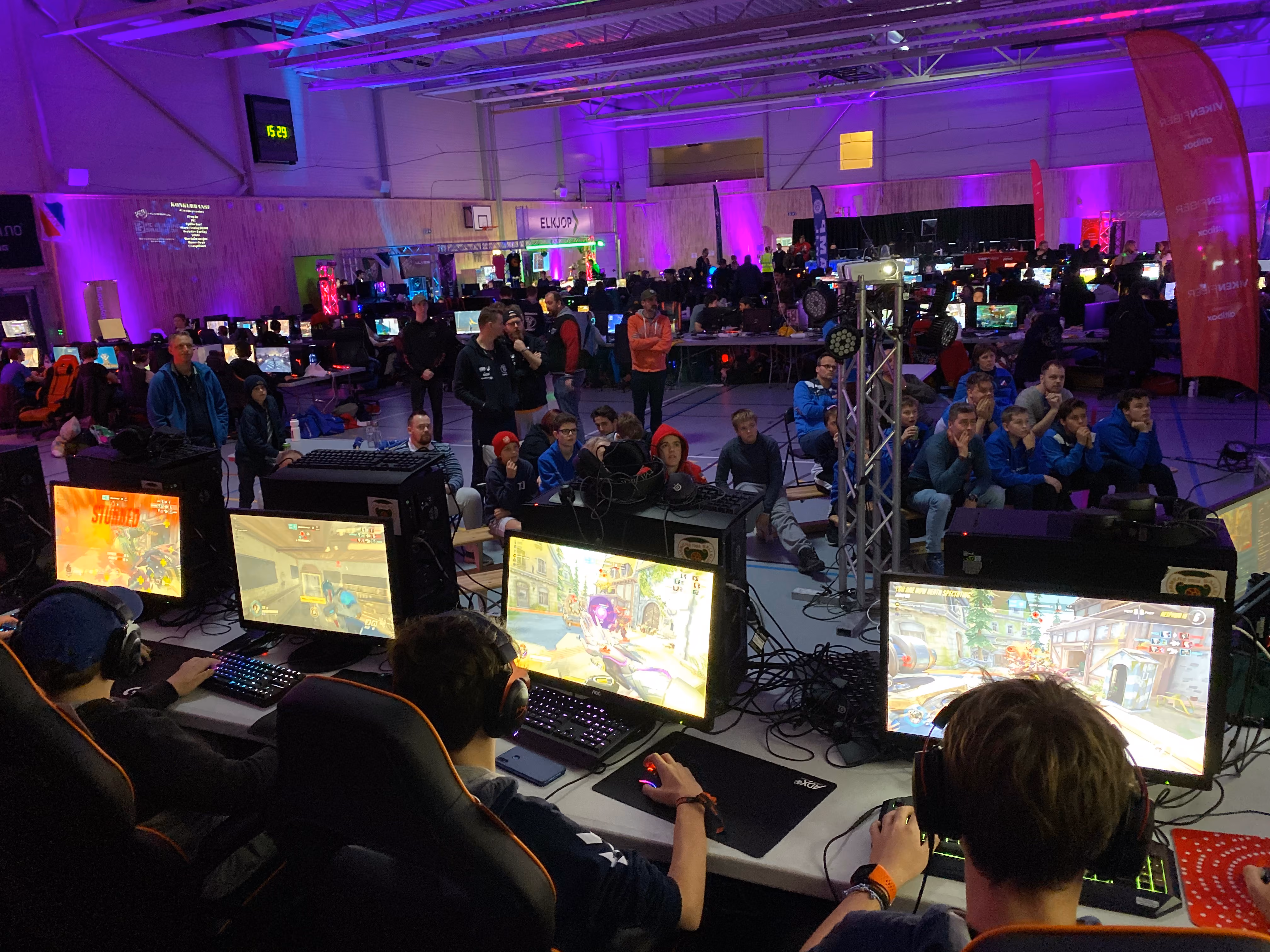 Ungdommer spiller dataspill på skjermer i en gaming-turnering med publikum i en stor hall.
