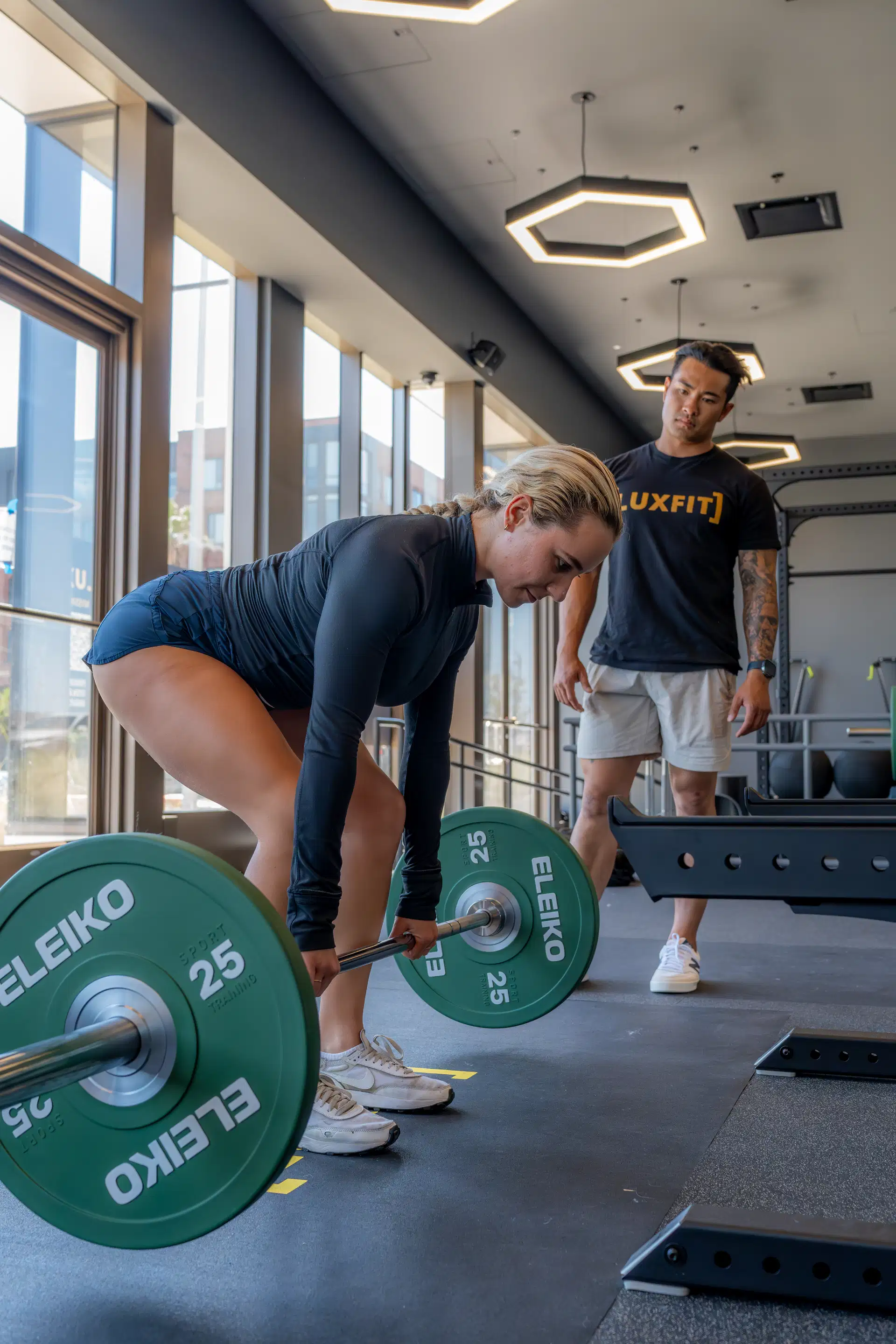 Athlete deadlifting with Eleiko plates while a Luxfit trainer coaches form in the gym.