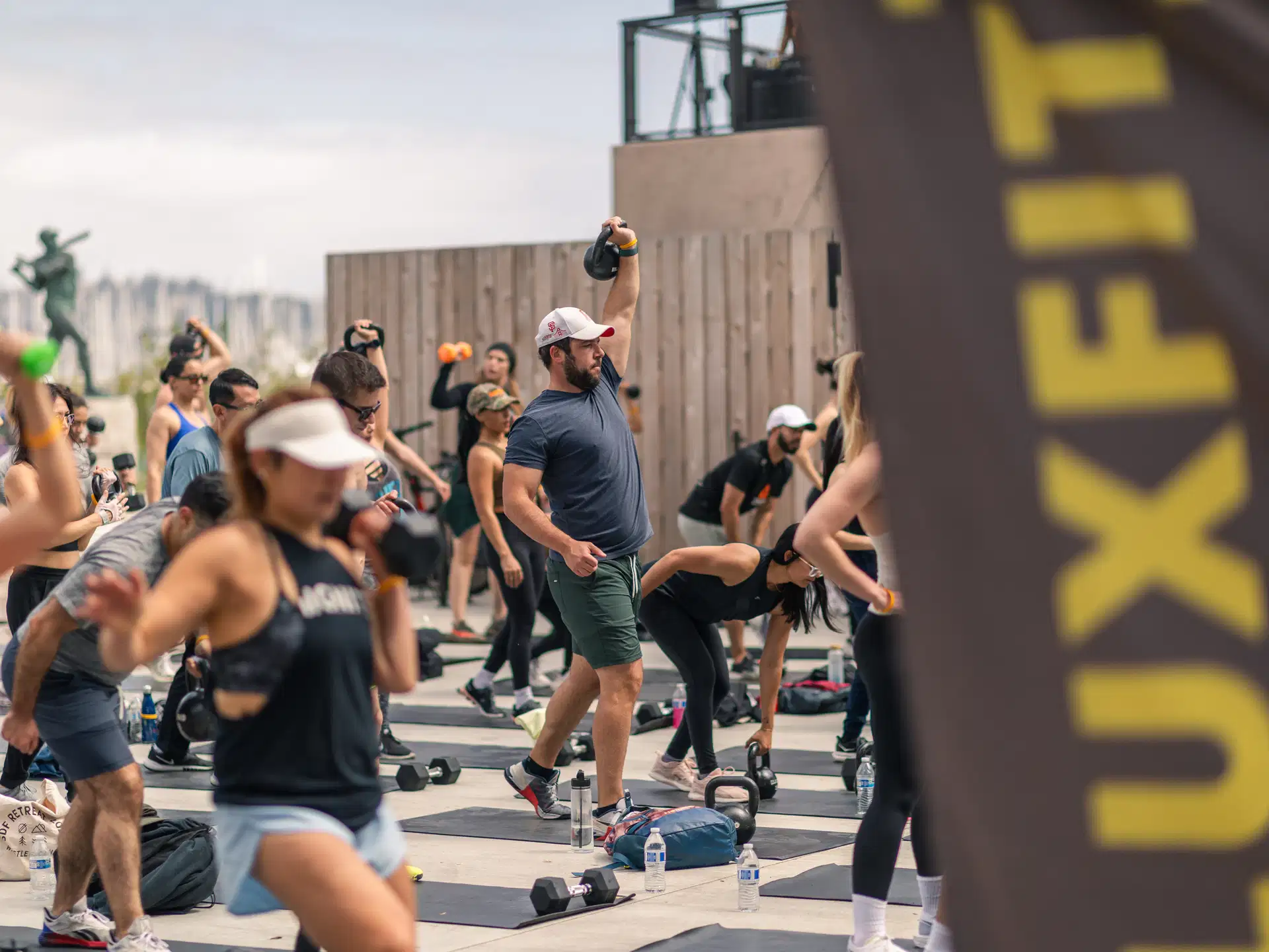 Outdoor Luxfit group fitness class with kettlebells and dumbbells under a Luxfit banner.