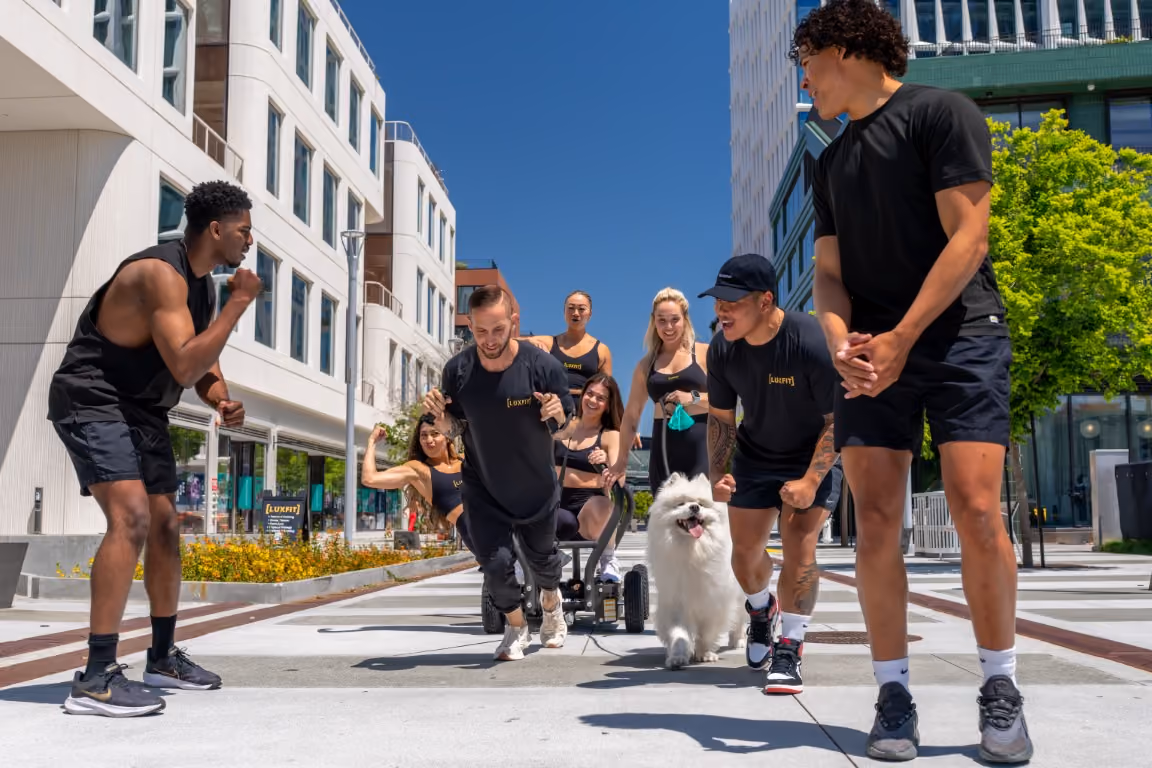 Luxfit members cheering during an outdoor sled-pull workout in a sunny urban plaza.