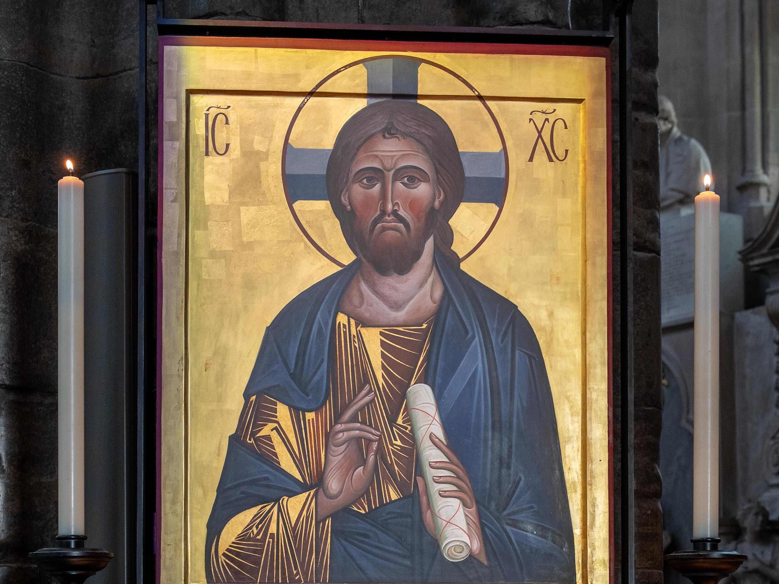 An icon of Jesus Christ with a gold background displayed between two lit candles inside Westminster Abbey in London, England.
