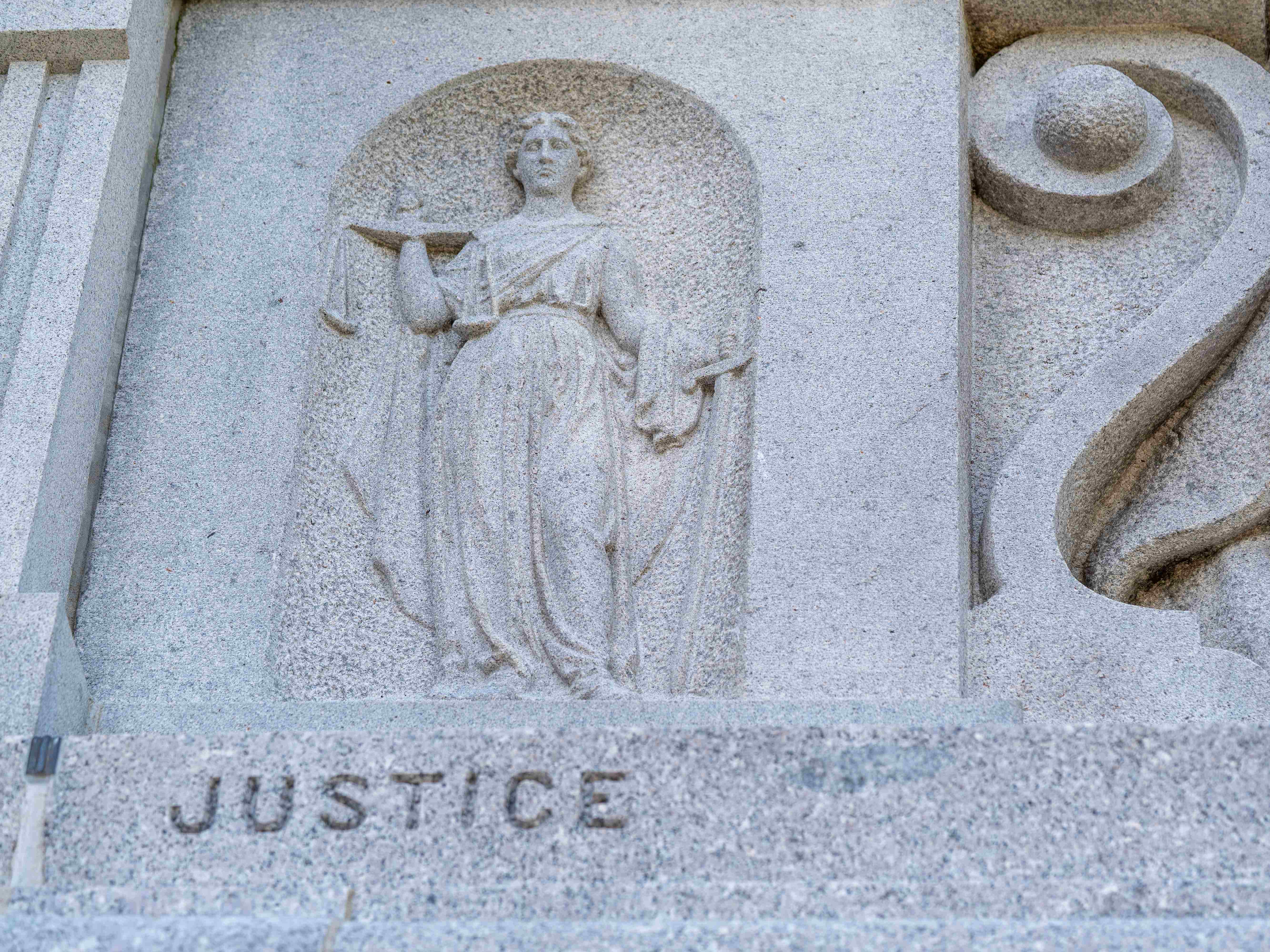 The allegorical figure of Justice carved into the National Monument to the Forefathers in Plymouth, Massachusetts, holding scales above the engraved word “Justice.”