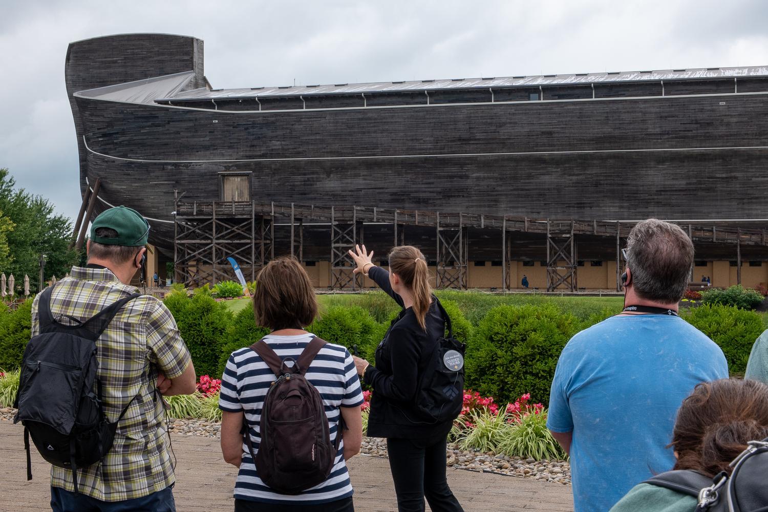 Inspire guide leads guests on a tour outside the Ark Encounter, pointing toward the life-size Noah's Ark as the group listens through wireless headsets.