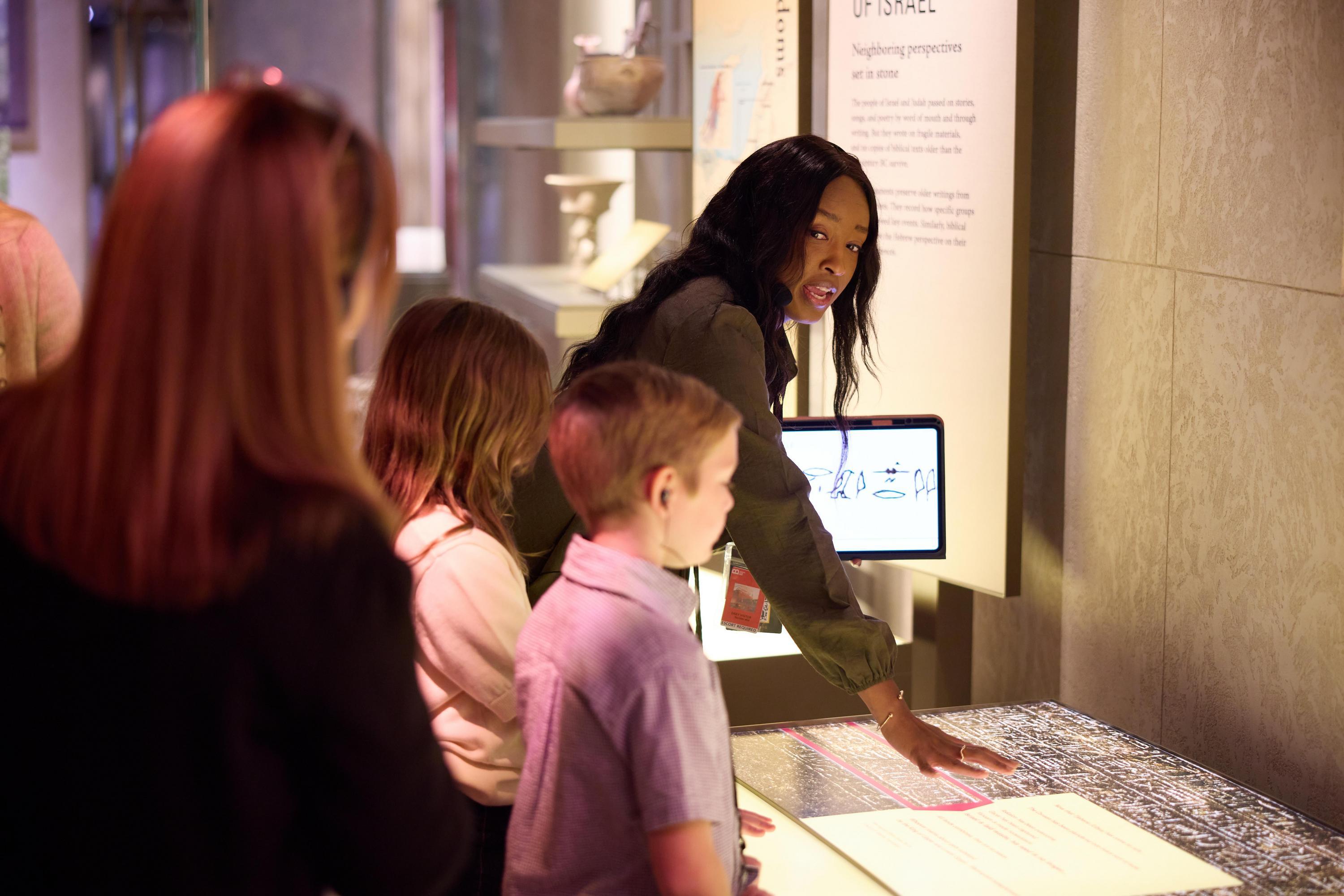 An Inspire guide leads guests through the Museum of the Bible, explaining an ancient inscription while displaying biblical Hebrew on a tablet.