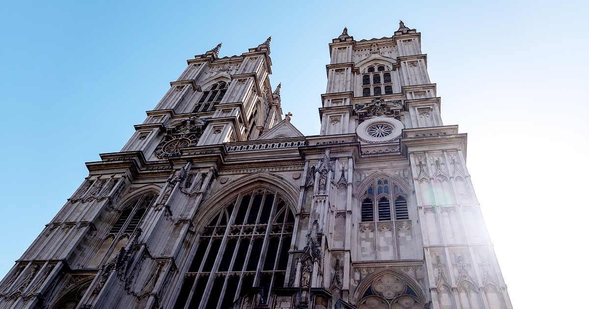Exterior view of Westminster Abbey in London, England, with its iconic Gothic towers rising against a clear blue sky.