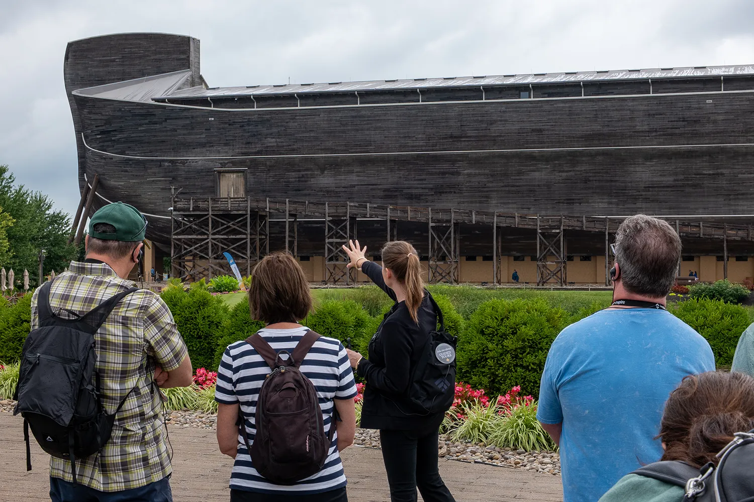 Inspire guide leads guests on a tour outside the Ark Encounter, pointing toward the life-size Noah's Ark as the group listens through wireless headsets.