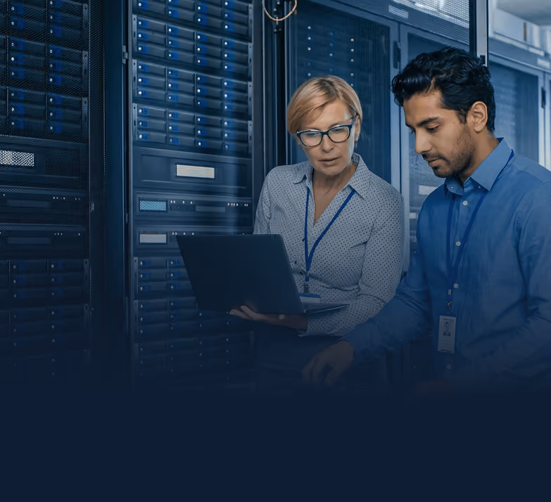 Two IT professionals working with servers, one holding a laptop and the other adjusting server equipment.