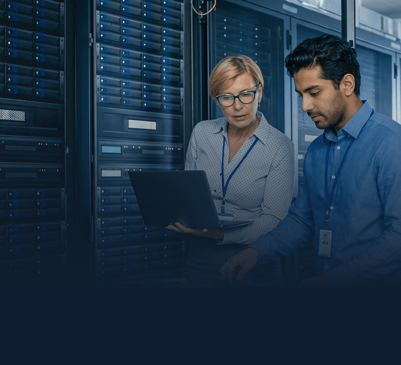 Two IT professionals working with servers, one holding a laptop and the other adjusting server equipment.