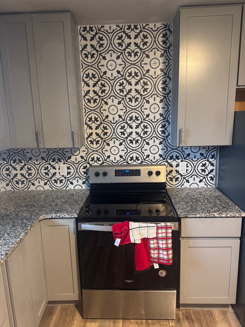 Finished kitchen range wall with a full-height patterned tile backsplash and granite countertops