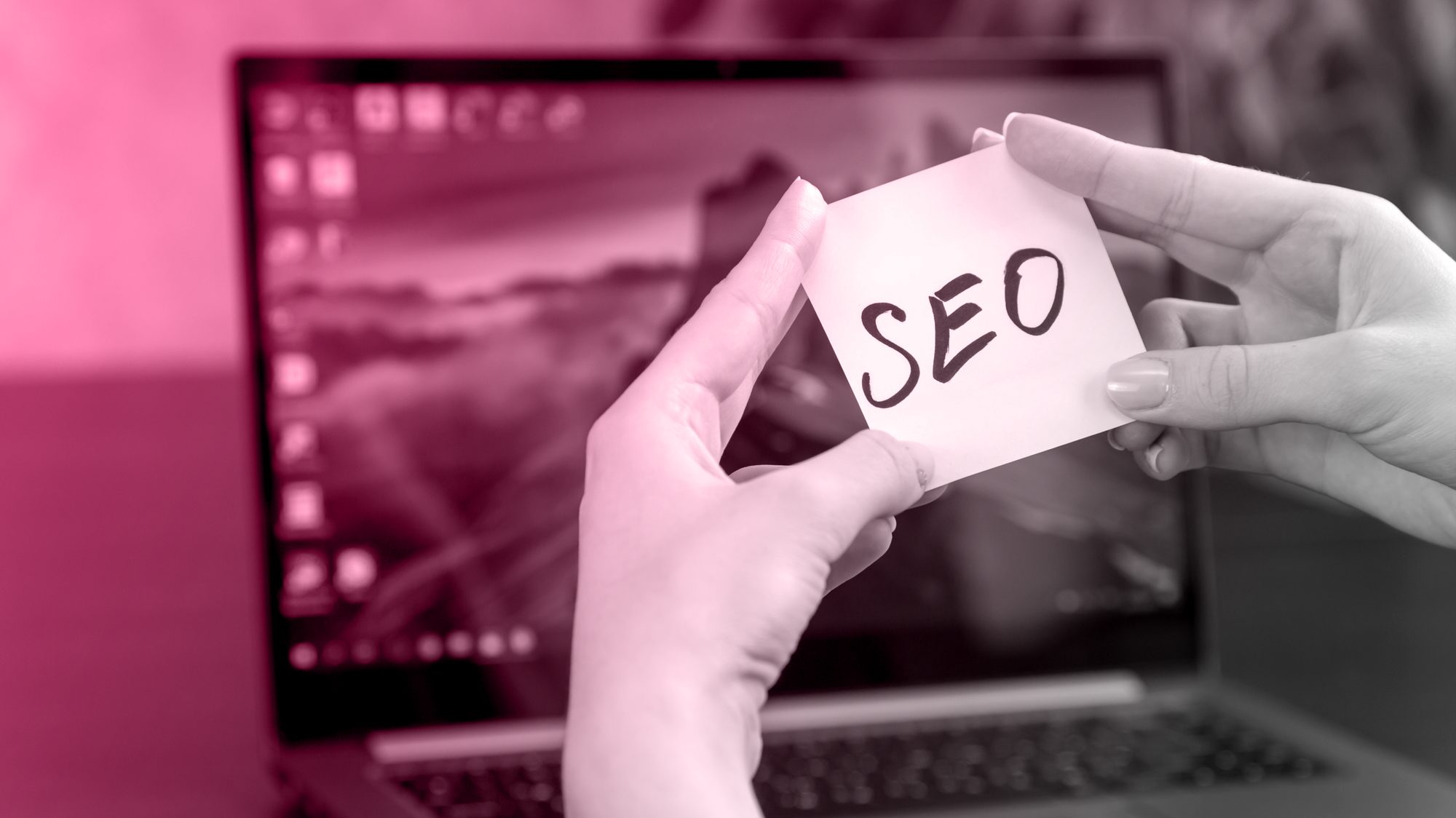 Hands holding a sticky note with SEO written on it in front of a laptop, illustrating off-page SEO strategy