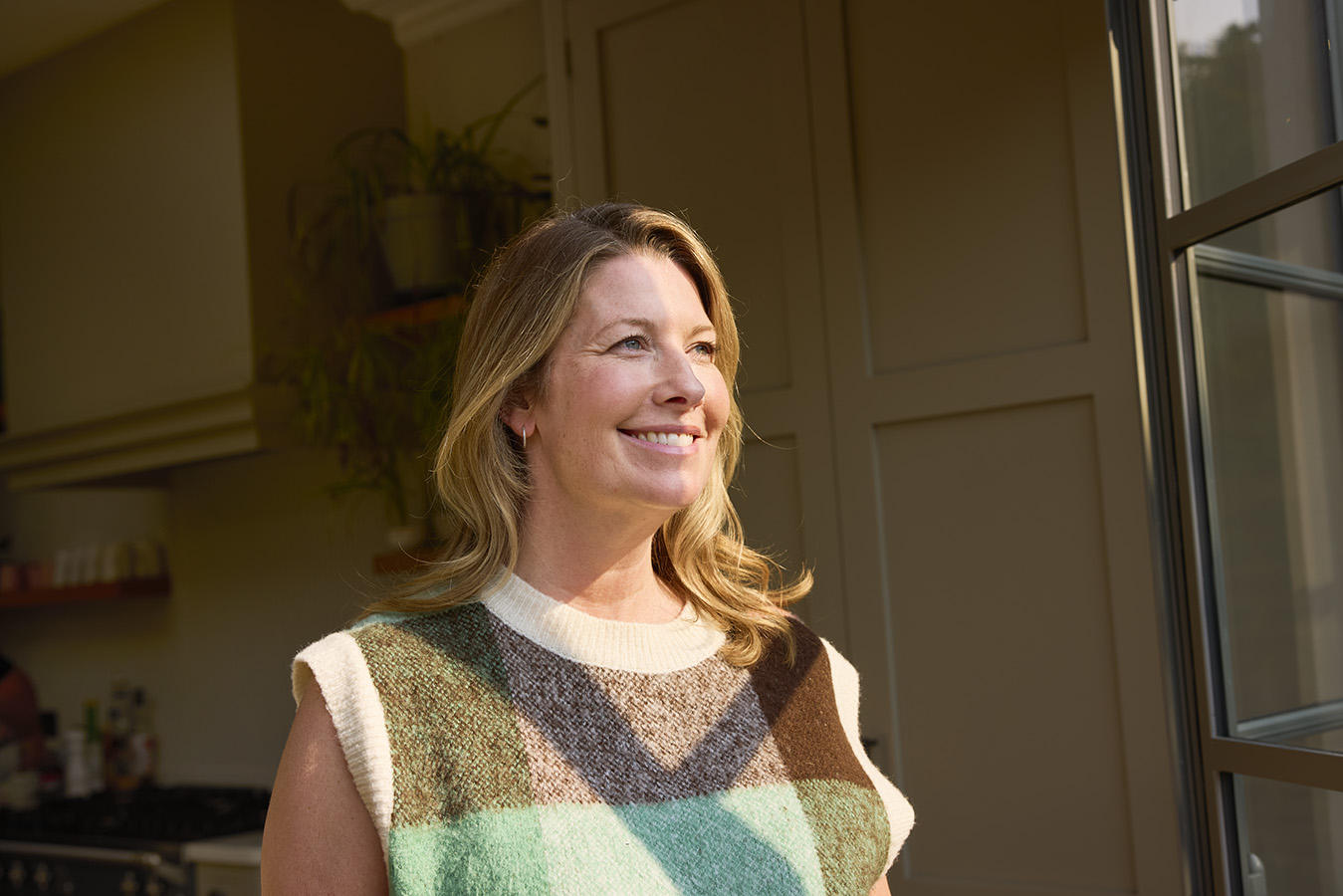 A woman in a knitted vest smiling in warm light
