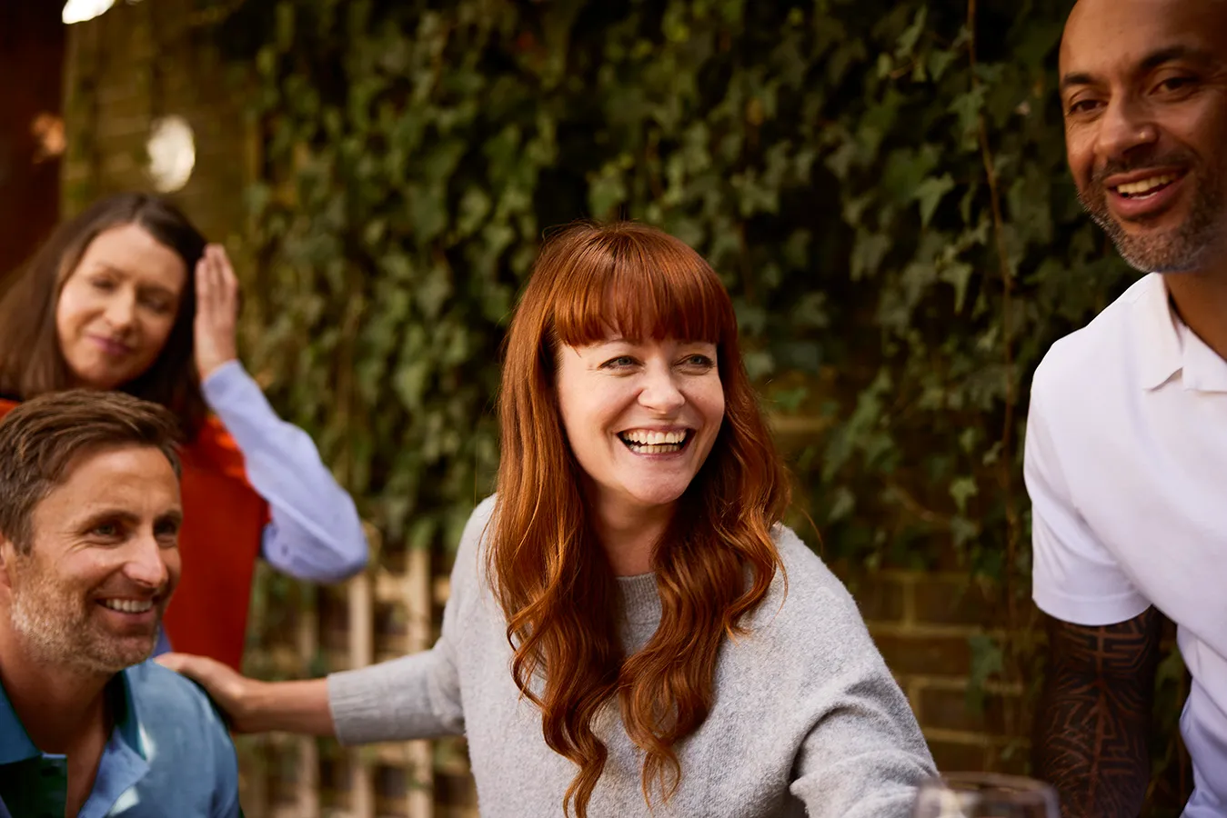A woman with red hair laughing with friends outdoors