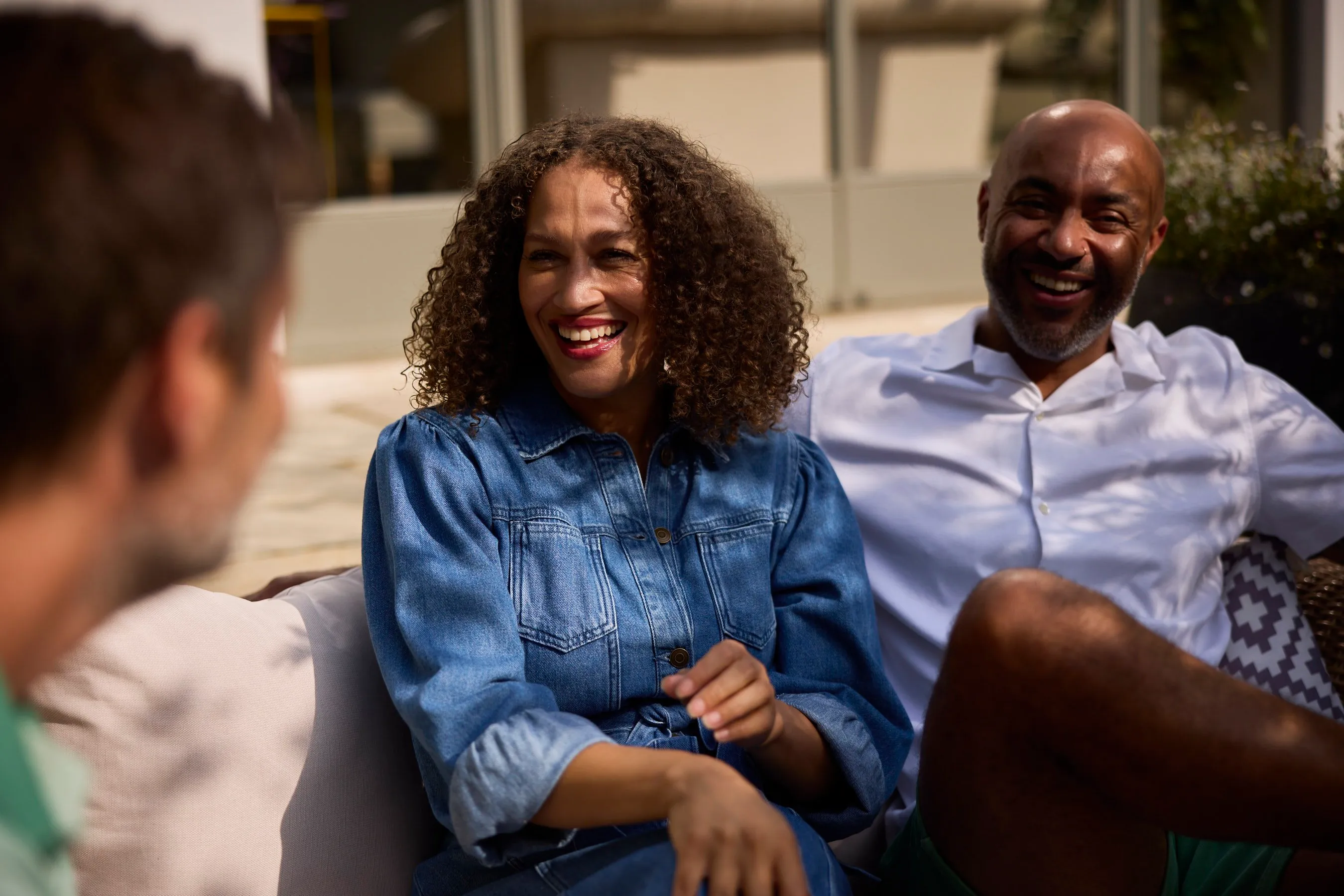 A woman in a denim shirt laughing with friends outdoors