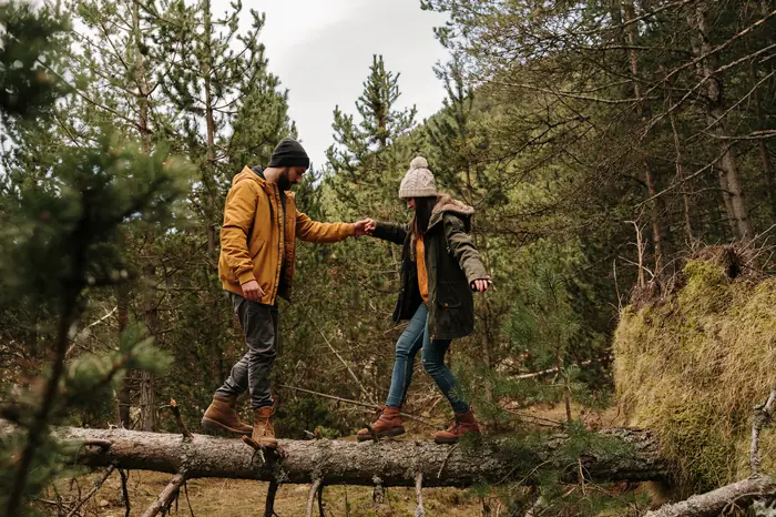 Two people balancing along a fallen log in woodland
