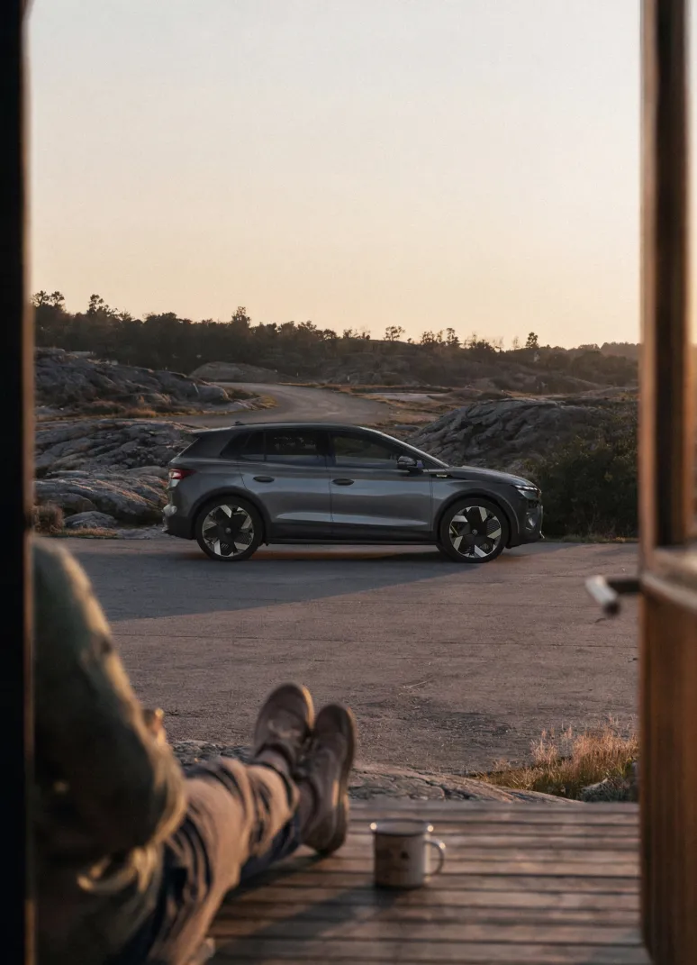 Harmaa sähköauto pysäköity kalliomaastossa hiekkatien vieressä auringonlaskun aikaan.