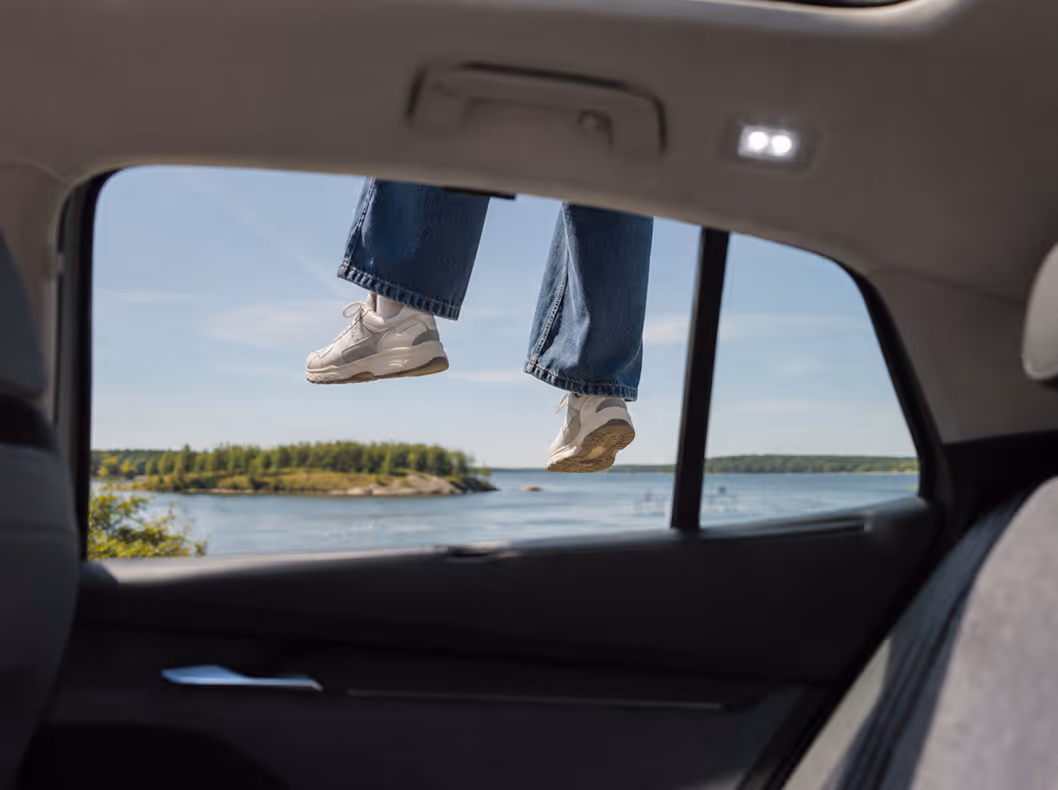 Ihminen roikkuu auton takaluukun aukon läpi, jalat roikkuvat taustalla olevan järven edessä.