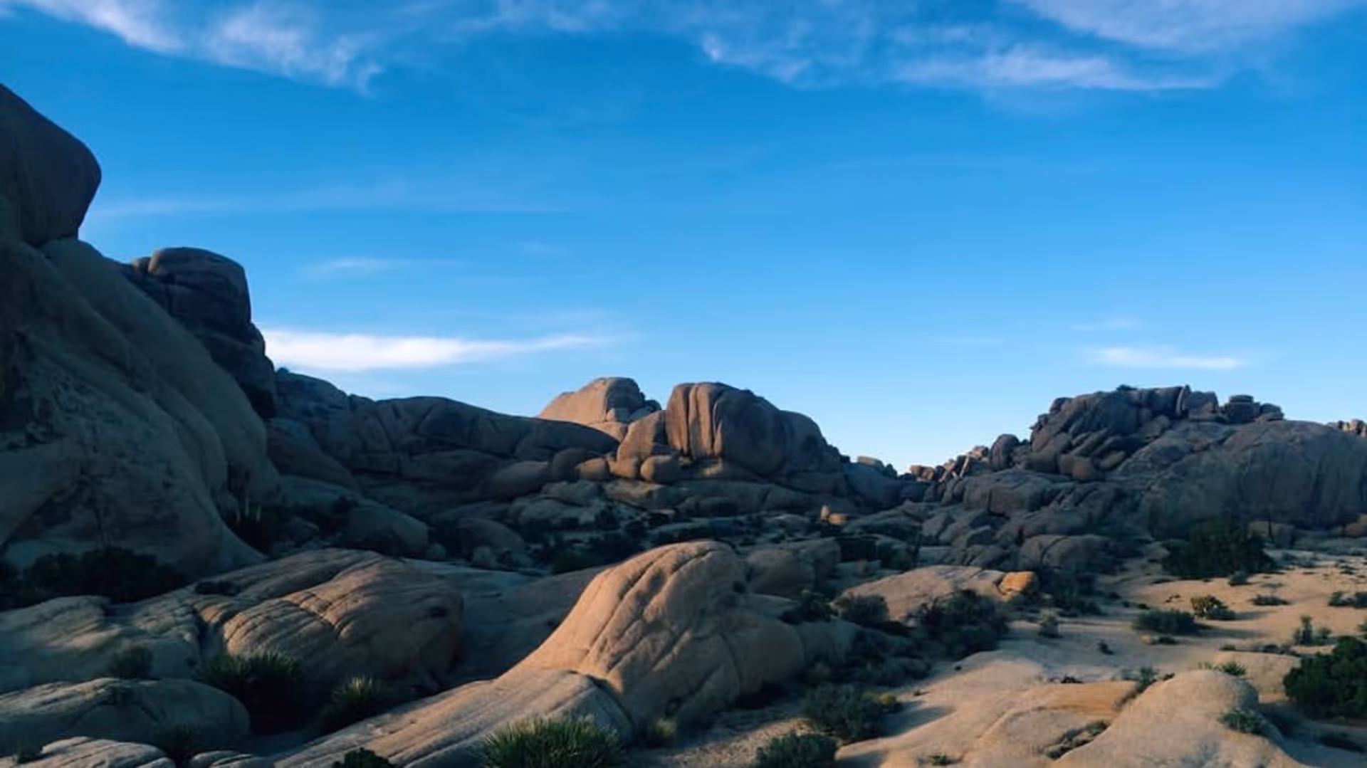 Rocky desert landscape with large boulders and sparse vegetation under a blue sky.