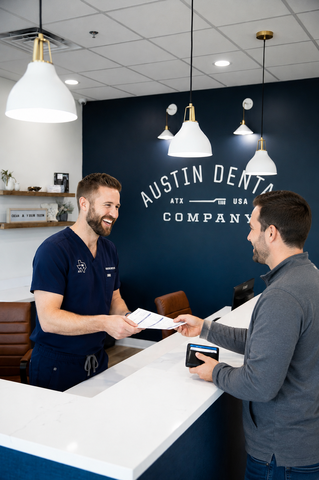 A friendly male patient receives paperwork from a smiling dental team member at a modern dental office reception desk, featuring a bright, welcoming lobby with pendant lighting and contemporary décor.