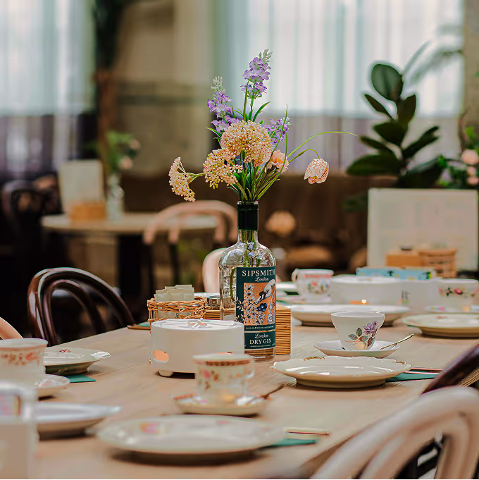 Dining table set with floral china and a gin bottle vase holding purple and peach flowers.