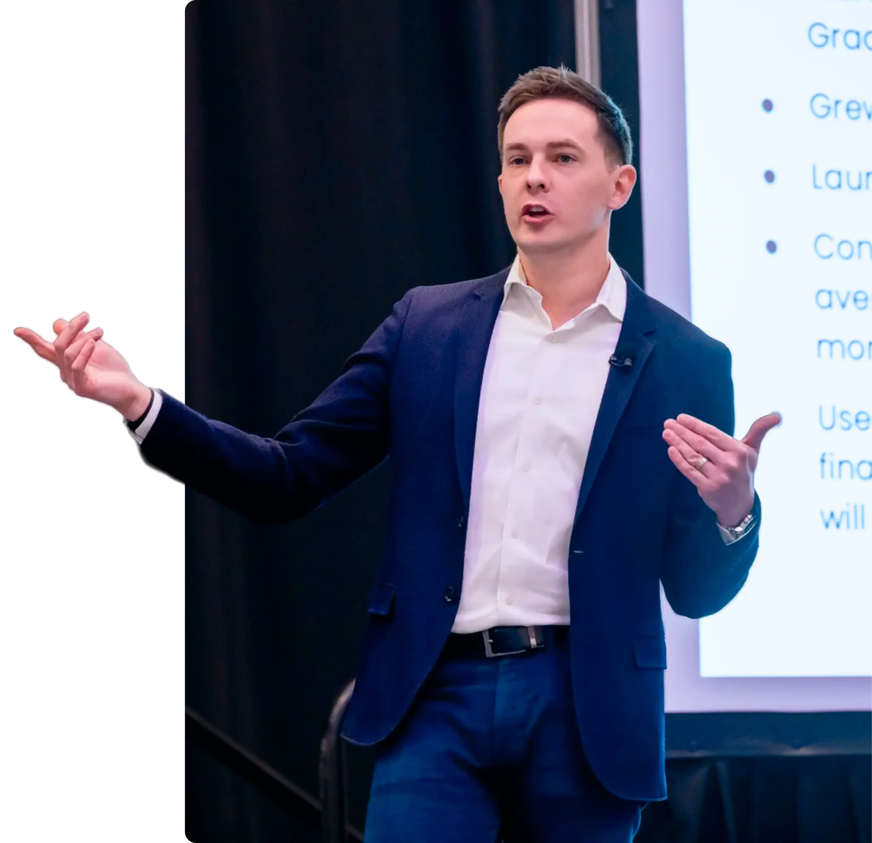 Man in navy suit presents with hand gestures in front of a screen showing bullet-point text.