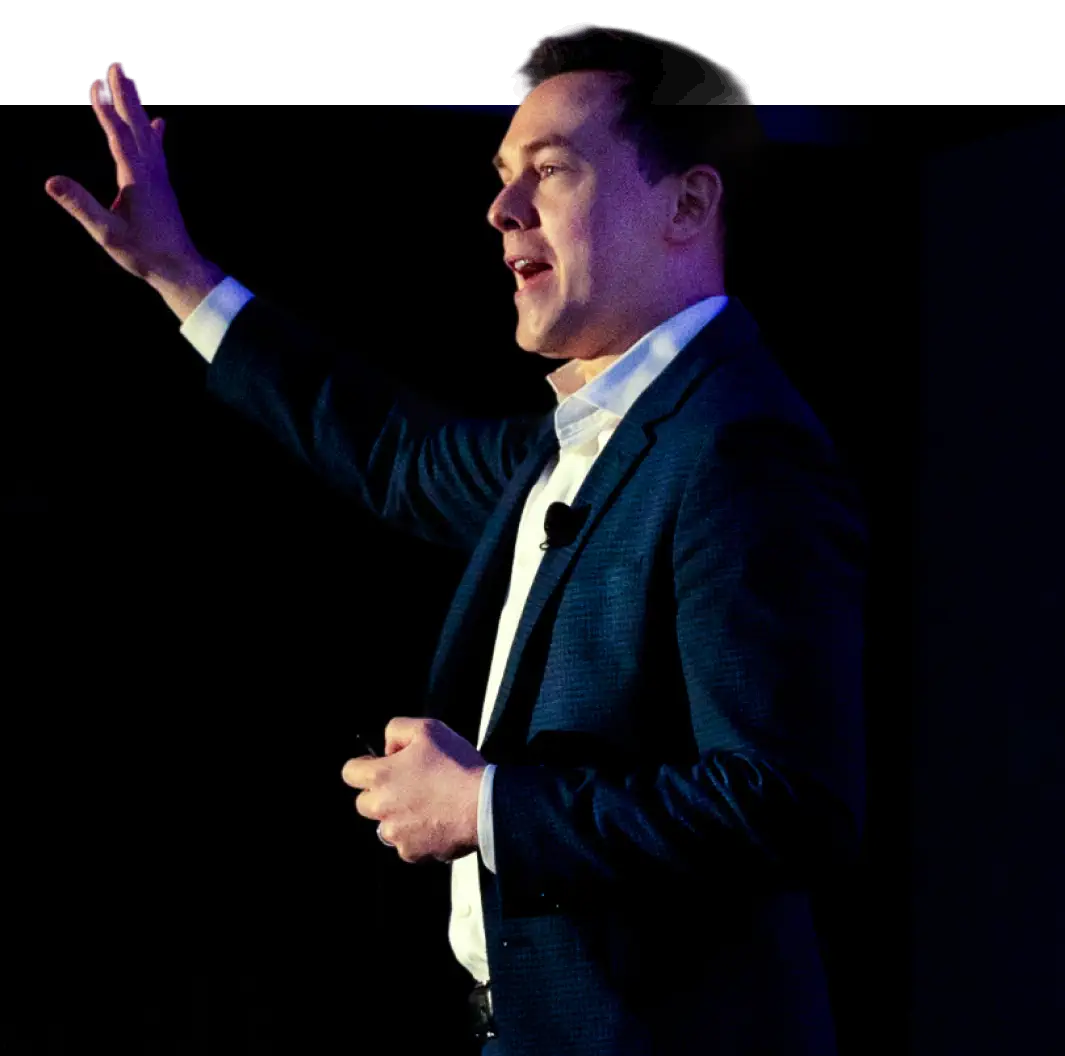 Kyle Scott in a suit speaking and gesturing with his hand raised on a dark stage.