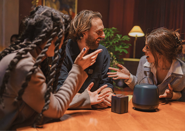 Three people sitting at a table engaged in a lively pocast conversation with a Nomono Sound Capsule on the table.