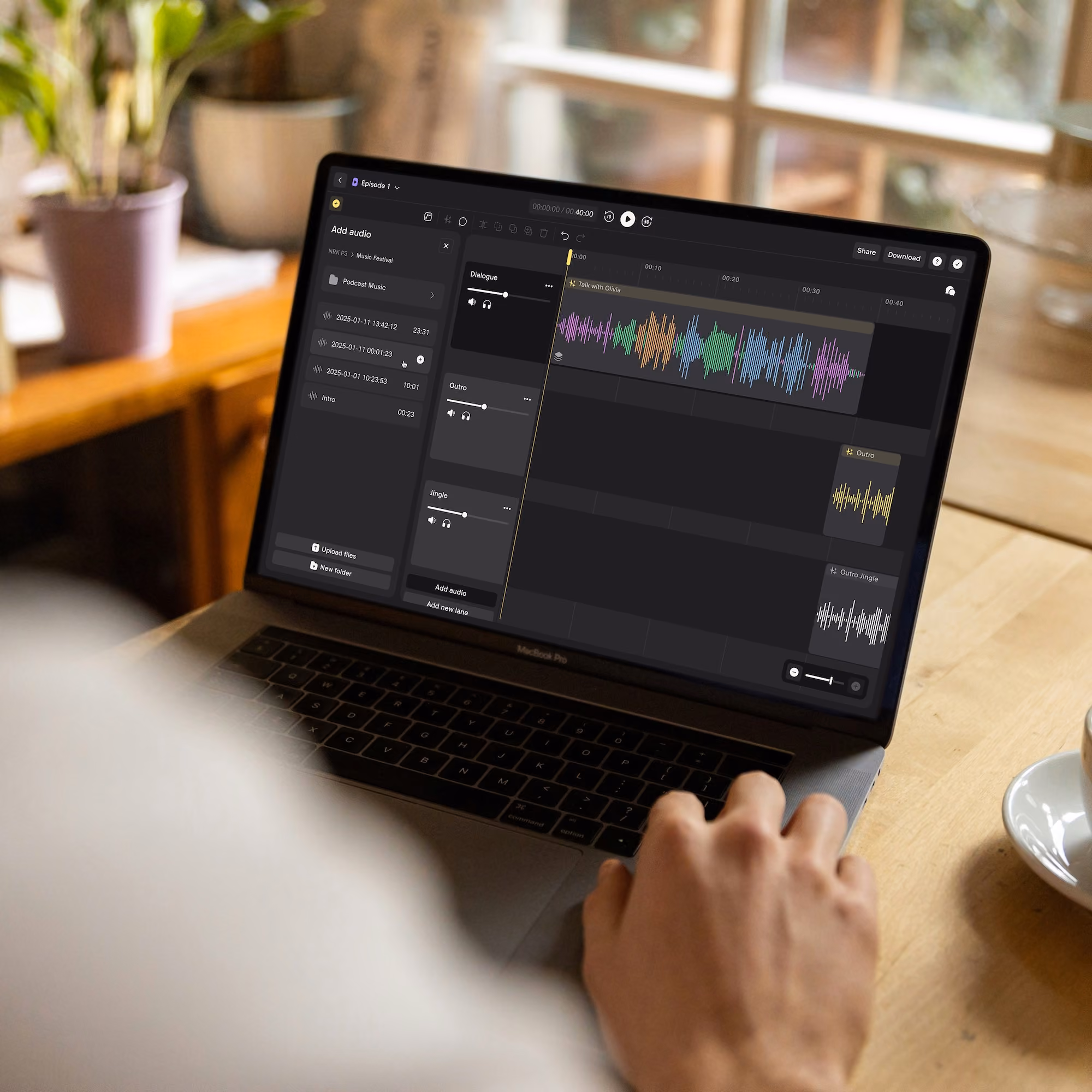 Person editing colorful audio waveforms on a MacBook Pro in a cozy room with plants and a coffee cup.