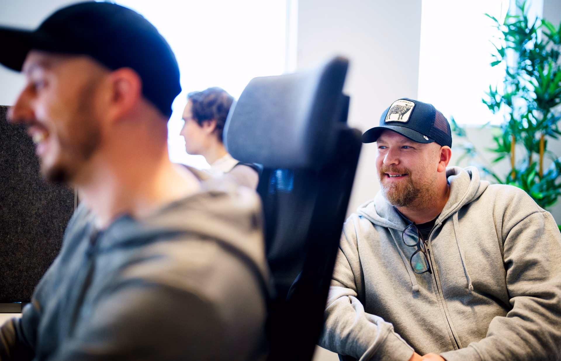 Three coworkers in casual clothes at desks in a bright office workspace.