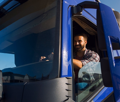 Smiling man wearing plaid shirt sitting in the driver's seat of a blue truck under clear sky.
