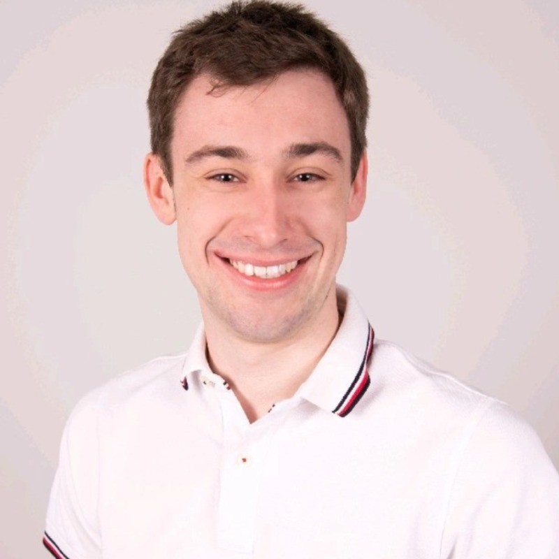 Smiling young man with short brown hair wearing a white polo shirt against a light background.