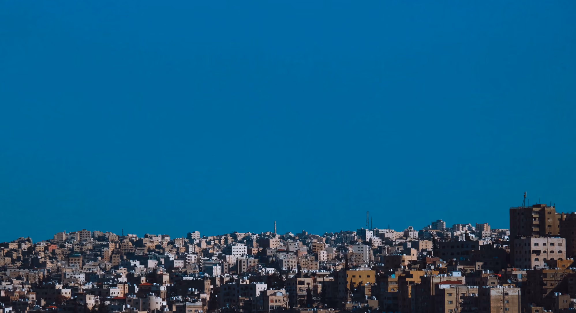 Cityscape with densely packed beige and light brown buildings under a clear deep blue sky.