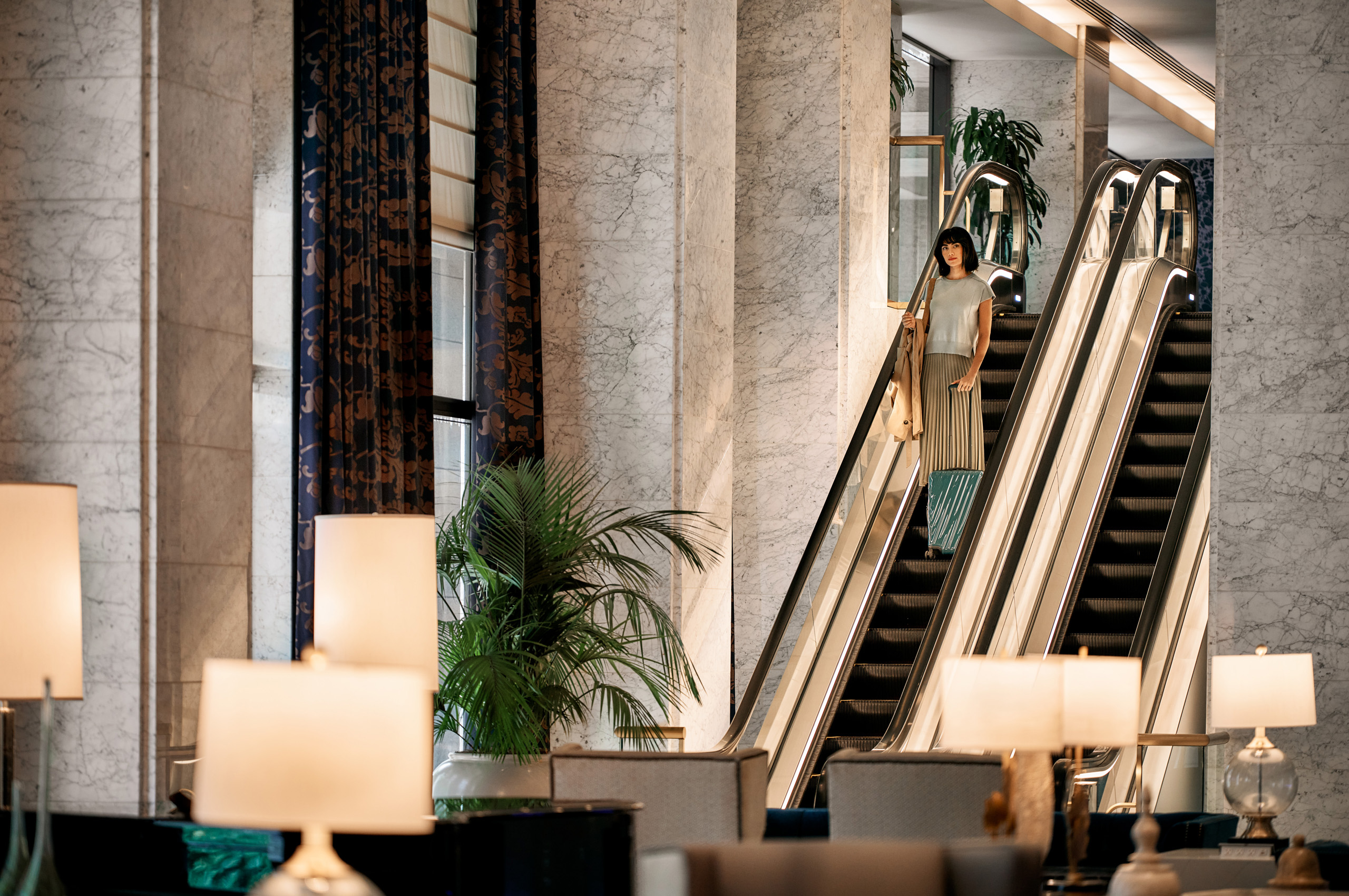 Guest descending escalator with rolling suitcase.