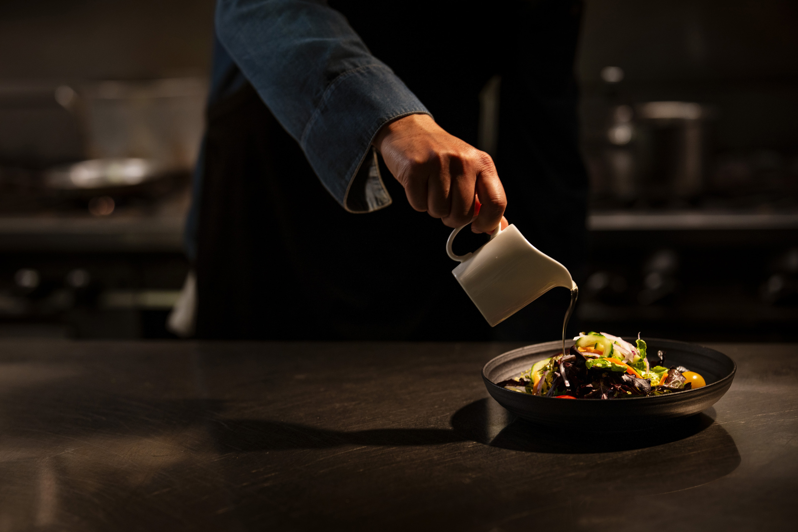 Chef pouring dressing onto fresh salad