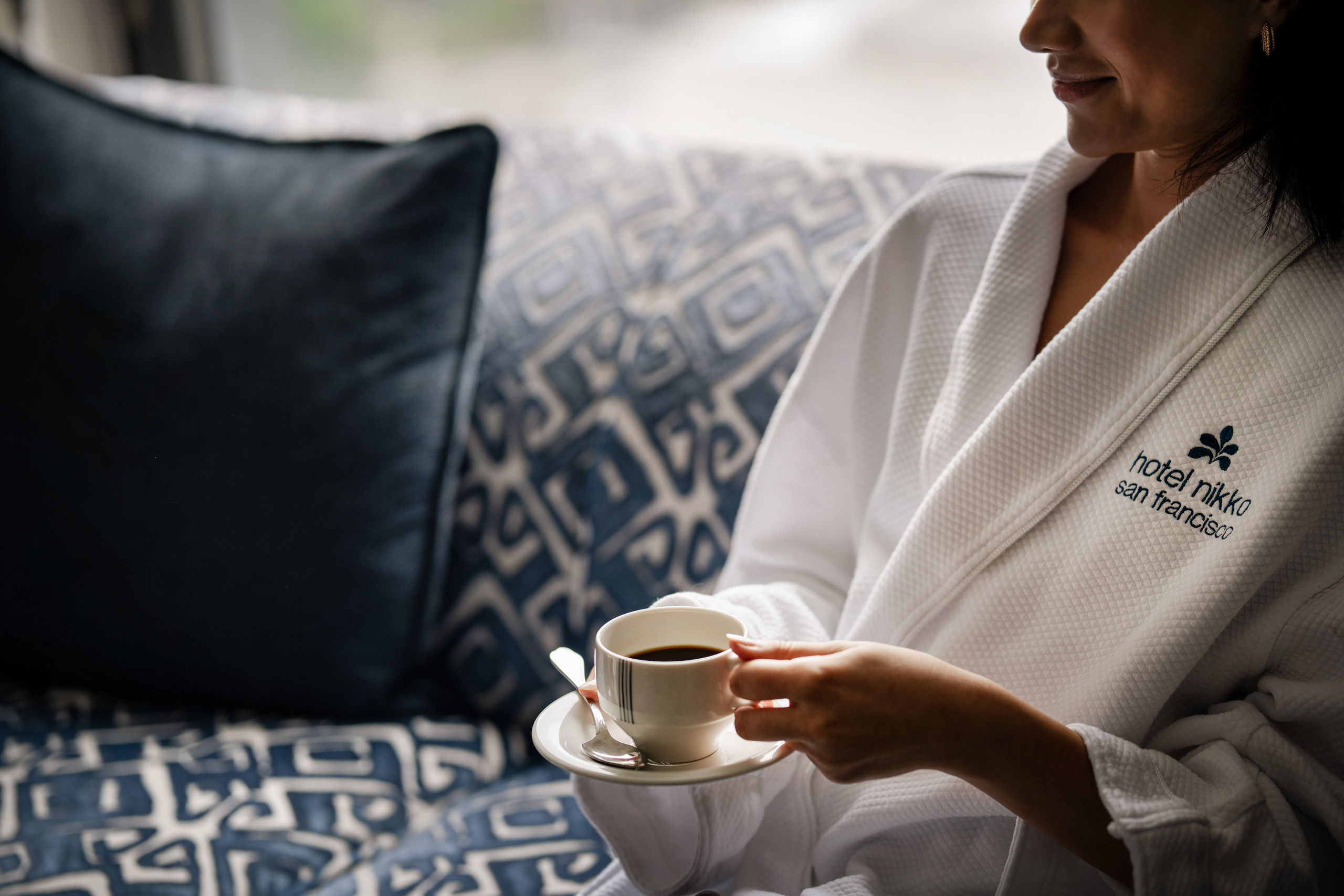 Guest in robe holding coffee cup on sofa