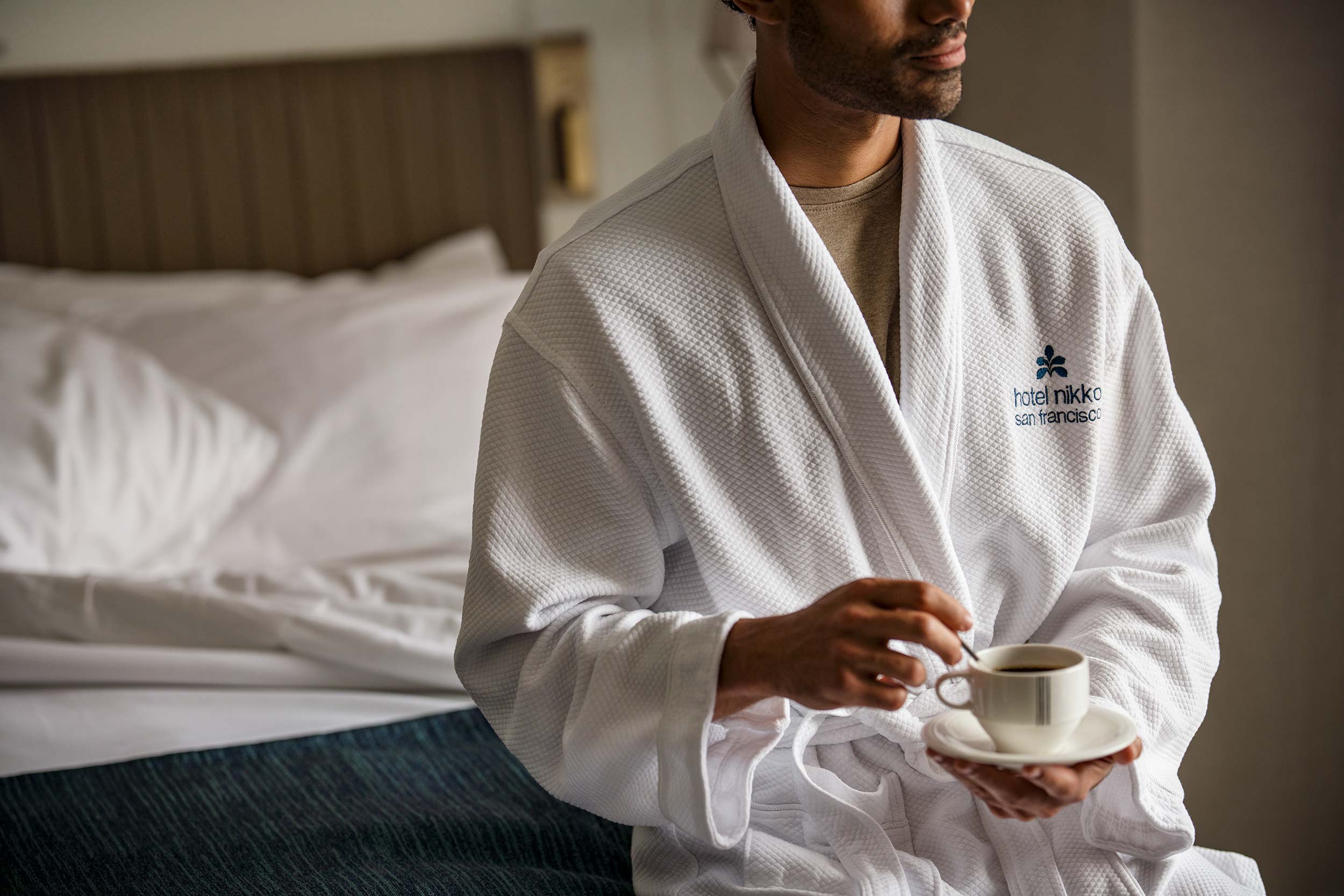Guest in robe enjoying coffee beside bed